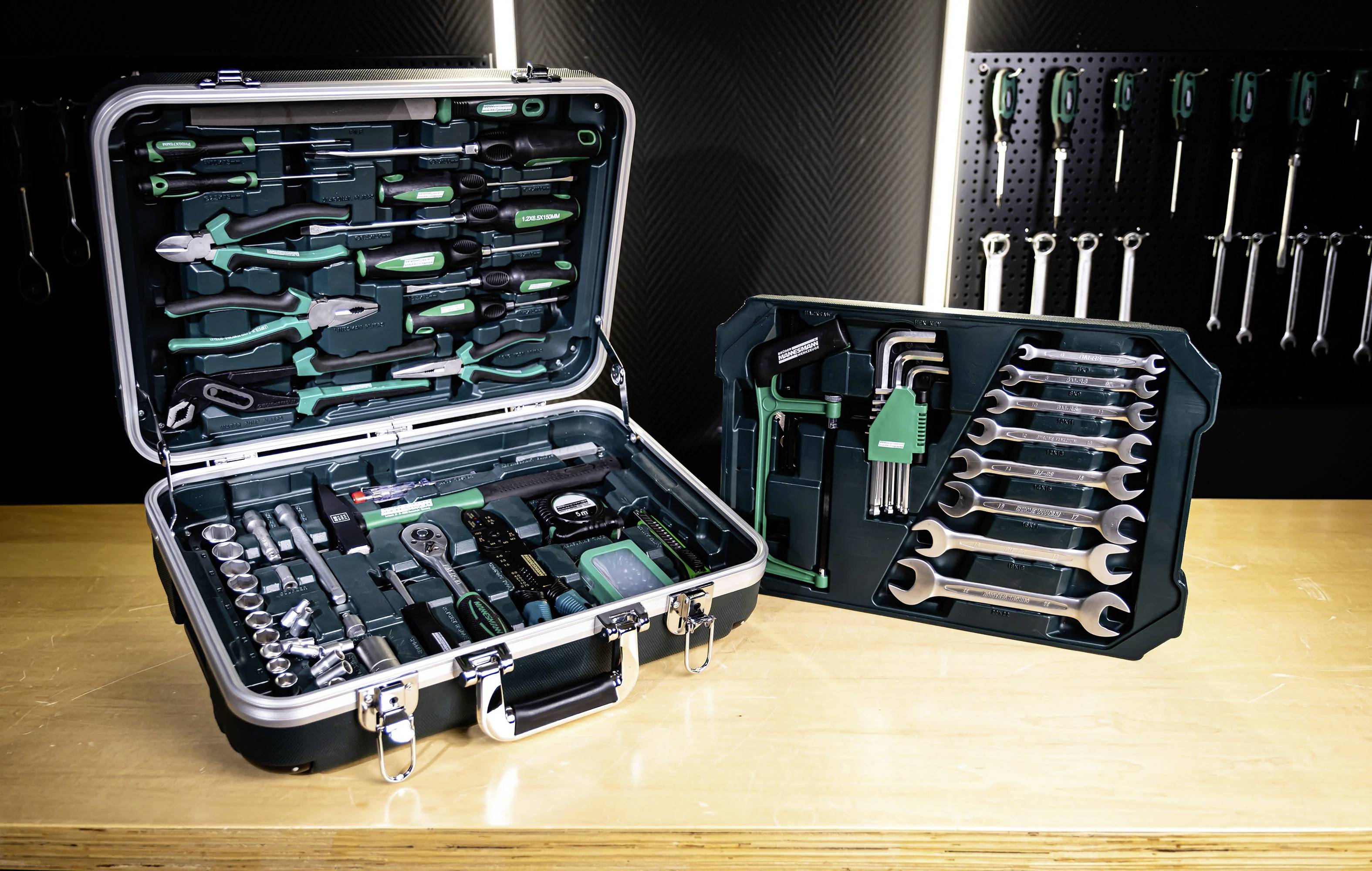 Werkzeugkästen mit verschiedenen Schraubenschlüsseln, Zangen, Steckschlüsseln und Schraubenziehern werden auf einer Werkbank ausgestellt. Eine Lochplatte hält zusätzliche Werkzeuge.
