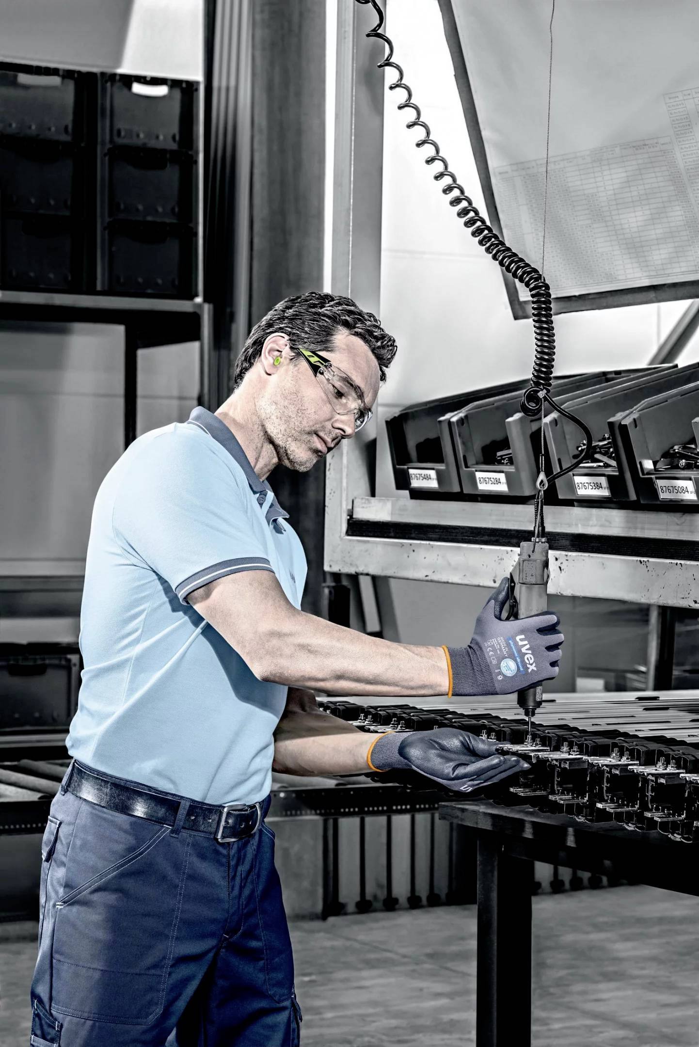 Mann in Werkstatt montiert mit Werkzeug Gerät an Arbeitsplatte. Trägt Schutzbrille und Handschuhe. Umgebung industriell.