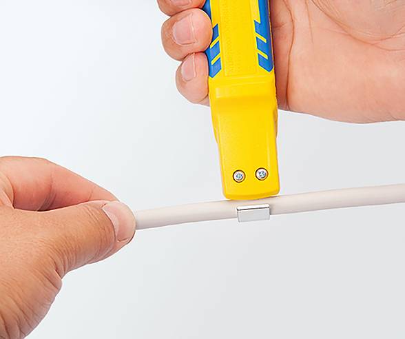 Eine Person verwendet ein gelbes und blaues Werkzeug, um ein weißes Kabel zu durchtrennen, wobei eine Nahaufnahme der Hände den Schneidvorgang fokussiert.