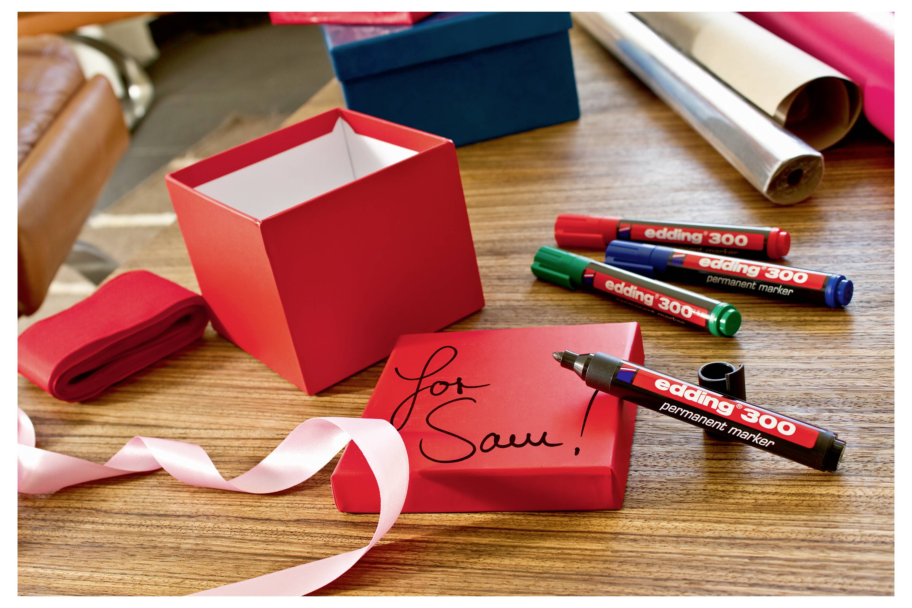 Rote Geschenkbox mit passendem Deckel mit der Aufschrift „Für Dich!" neben einem Band und mehreren farbigen Stiften auf einem Holztisch.