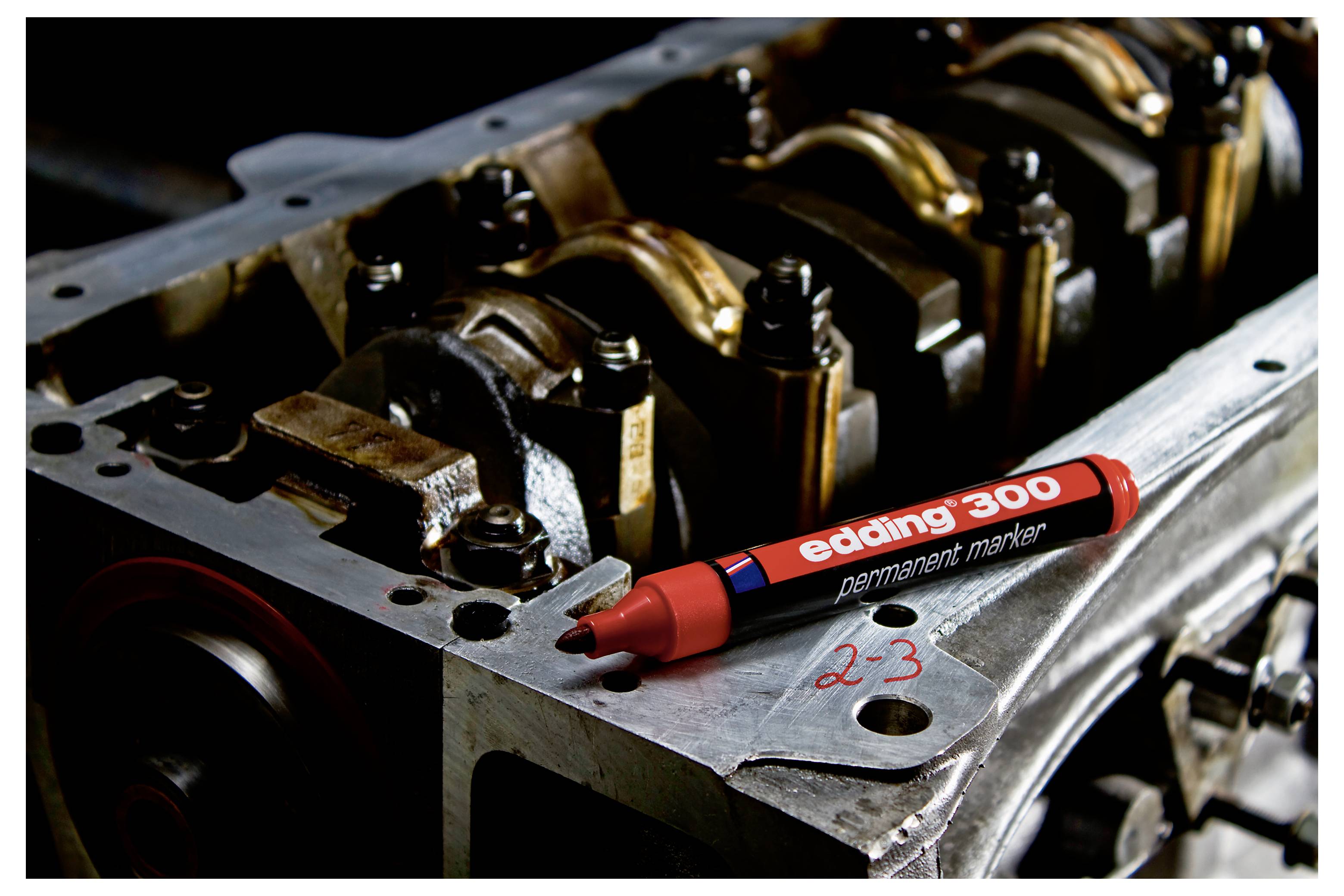 Roter Permanentmarker mit der Bezeichnung "edding 300" auf einem Metallteil eines Motors oder einer Maschine mit Bolzen und einer handschriftlichen Markierung "2-3".