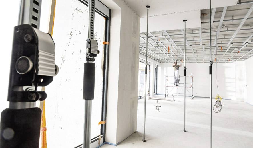 Innenansicht eines Gebäudes in Renovierung, mit Deckenstützen und einem Arbeiter auf einem Gerüst, der an der Decke arbeitet.