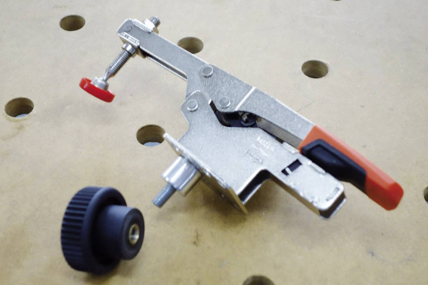 Metallspanner mit rotem und schwarzem Griff zur Befestigung von Werkstücken auf einer Werkbank.