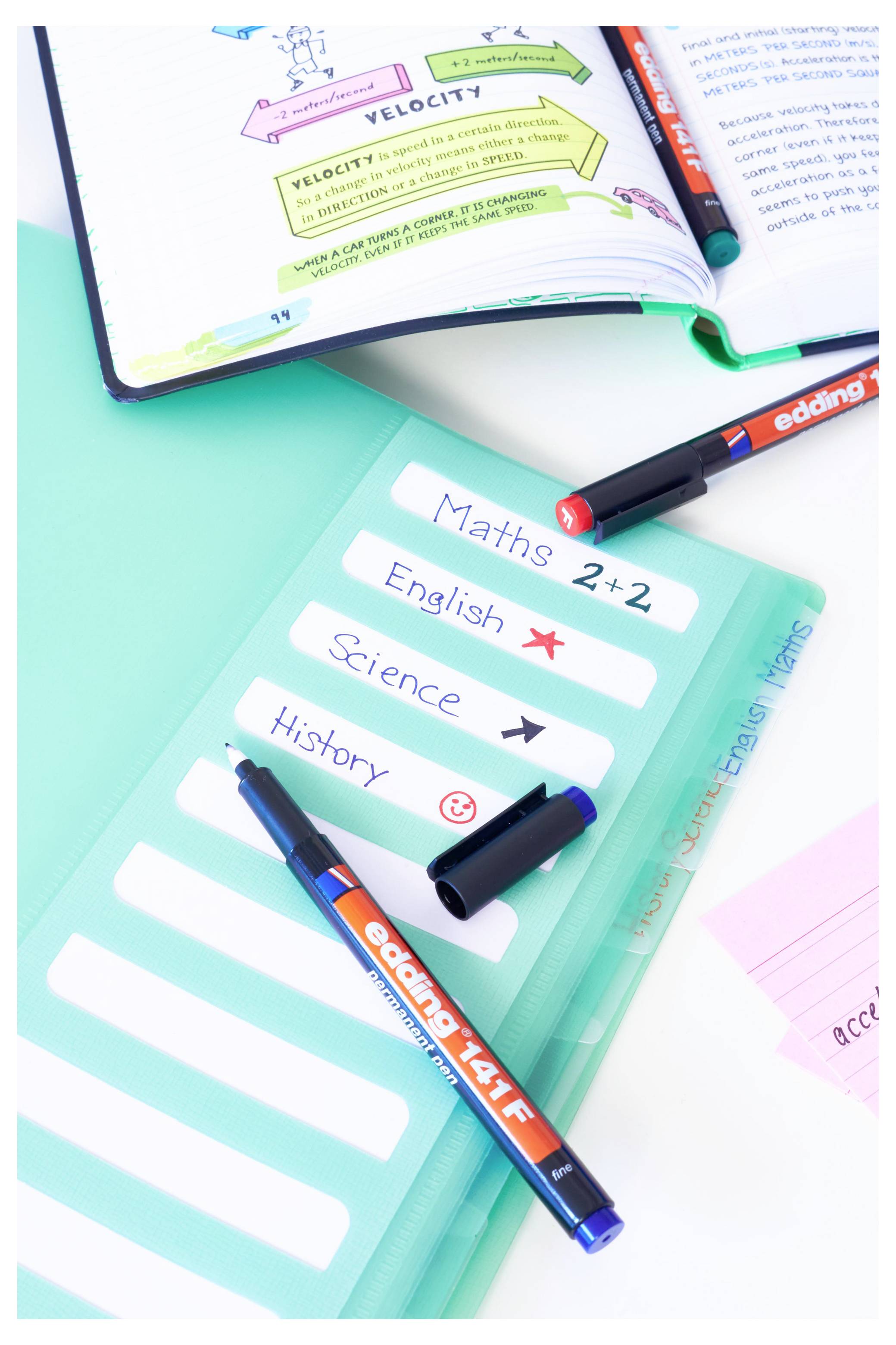 Ein Schularbeitsheft und Planer auf einem Schreibtisch, mit farbigen Fachlabeln wie 'Mathematik 2+2', 'Englisch', 'Naturwissenschaften' und 'Geschichte' neben Stiften und einem Notizbuch.