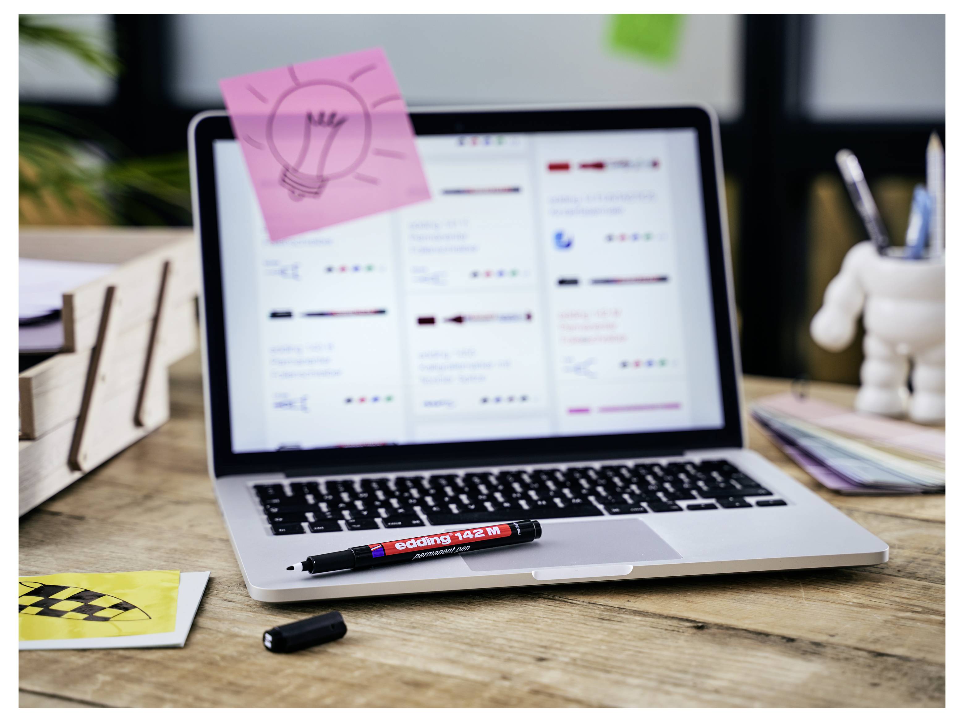 Laptop mit einem Projektplanungs-Dashboard auf einem Schreibtisch angezeigt, mit einer Glühbirnen-Haftnotiz, Marker und Büroartikeln herum.