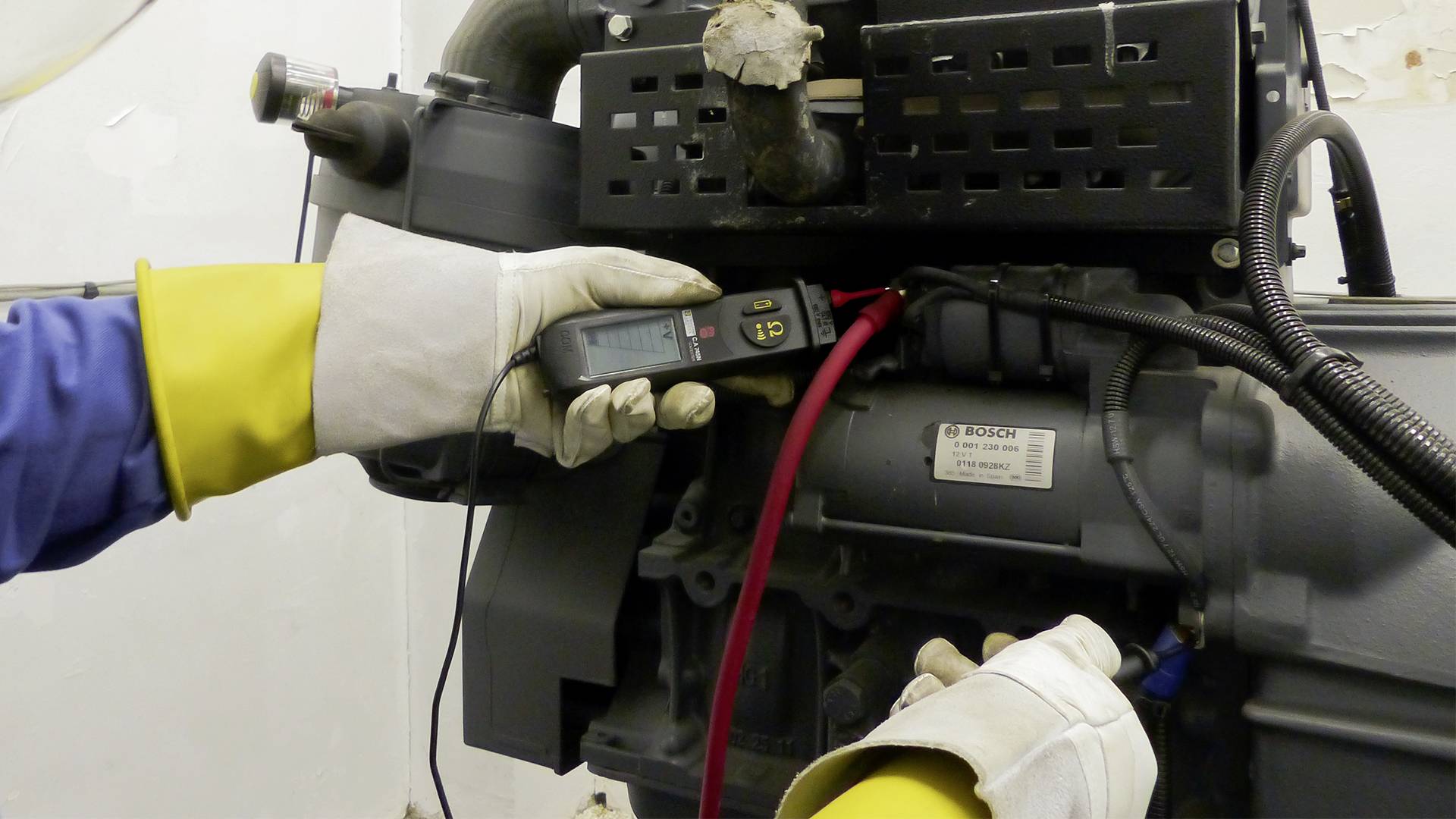 Ein Techniker misst elektrische Werte an einer Maschine mit einem Multimeter. Aufkleber mit technischen Angaben sind auf der Maschine sichtbar.