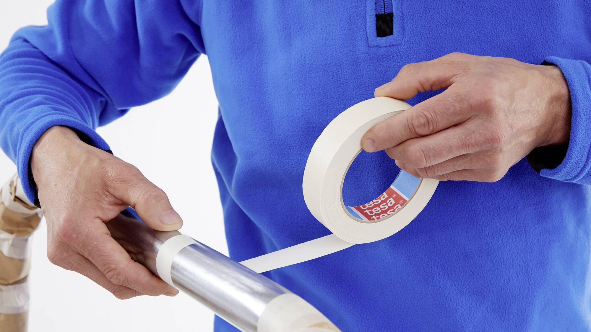 Person in blauem Pullover umwickelt eine Metallstange mit weißem Klebeband.
