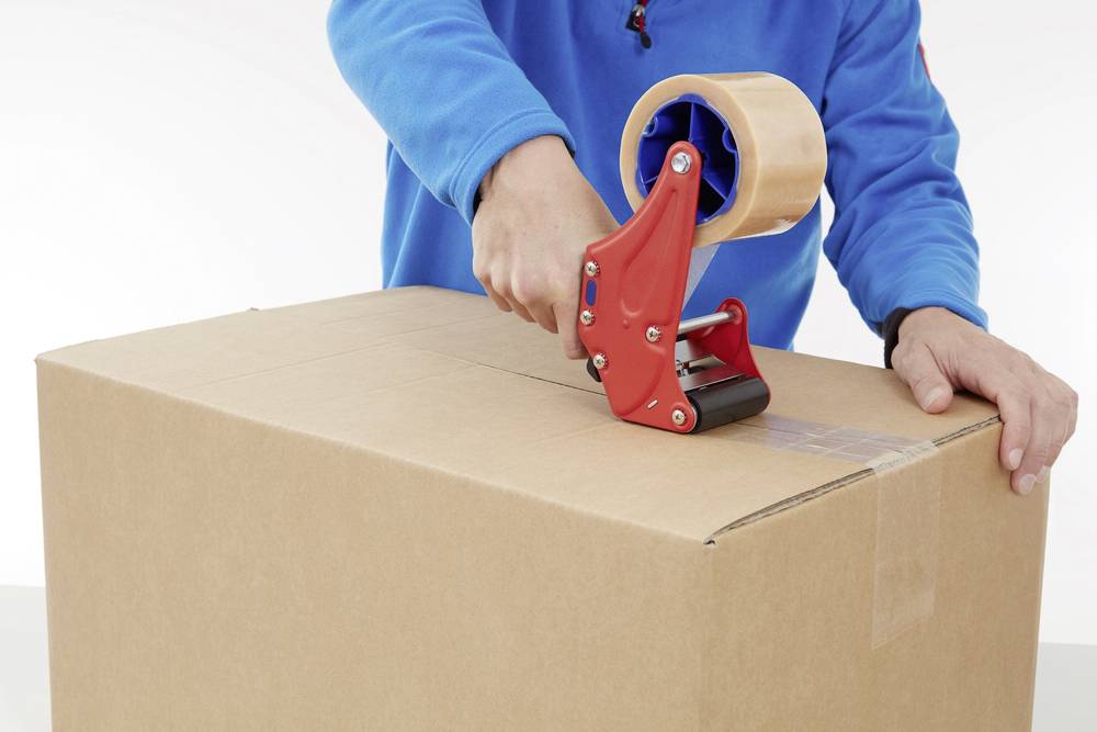 Person verpackt einen Karton mit einem Klebebandabroller.