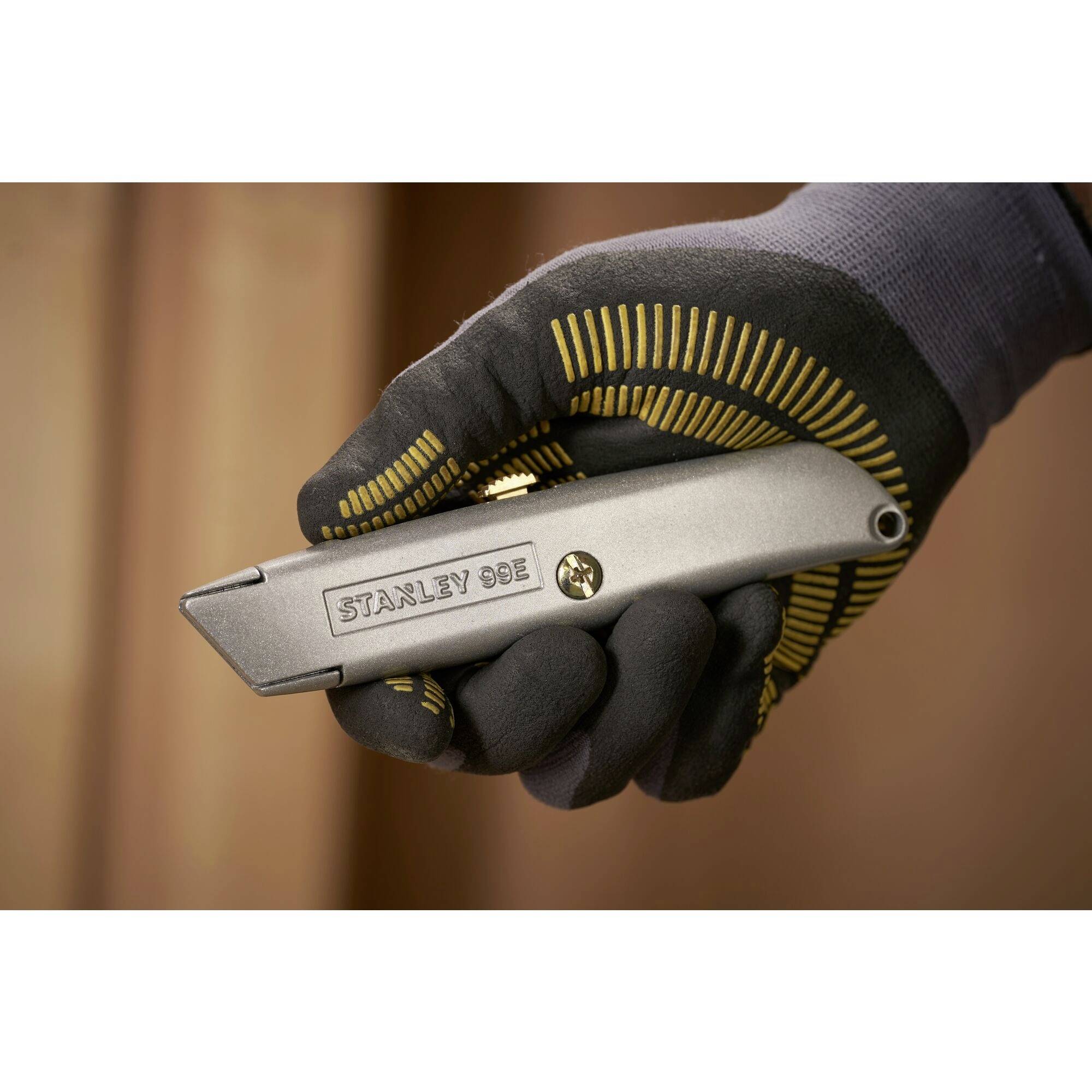 Hand in schwarzem Handschuh hält ein silbernes Stanley 99E Cuttermesser vor unscharfem Hintergrund.
