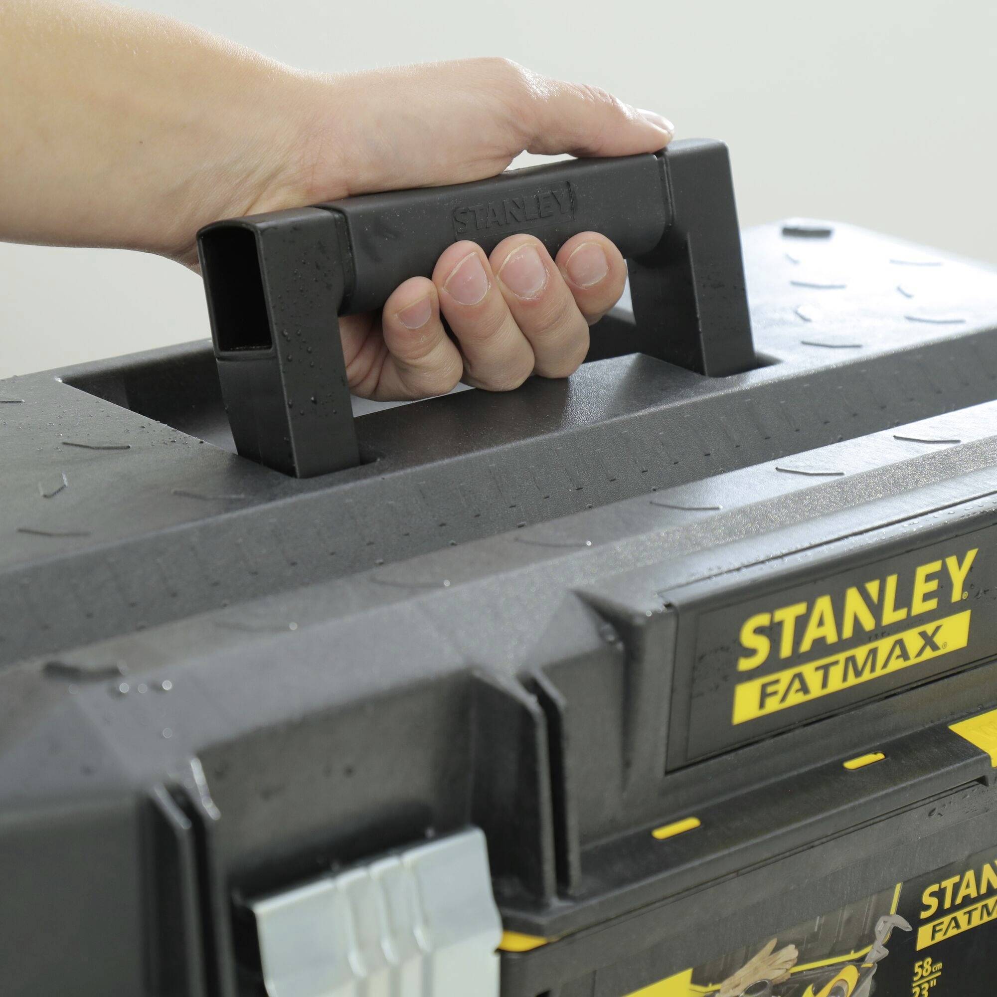 Eine Hand hält einen schwarzen Werkzeugkasten mit 'Stanley Fatmax'-Logo, der aus Kunststoff gefertigt ist.