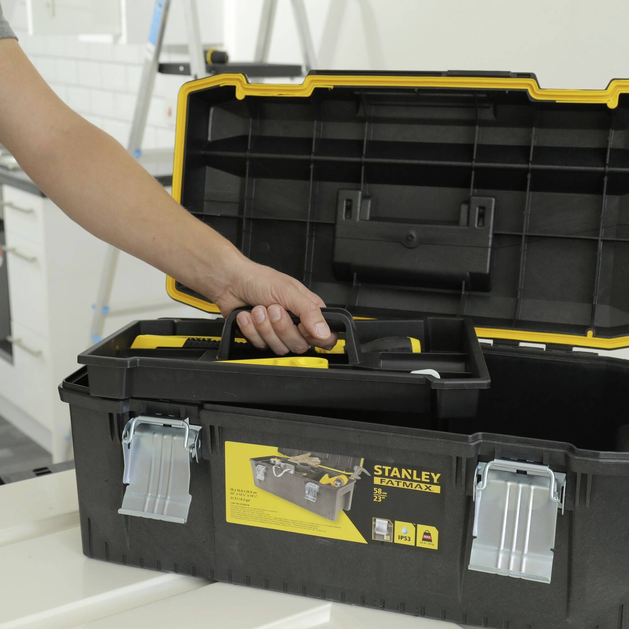 Eine geöffnete schwarze Werkzeugbox auf einem Tisch in einer Küche, mit Werkzeugen hinein gelegt, eine Hand hält den Griff.