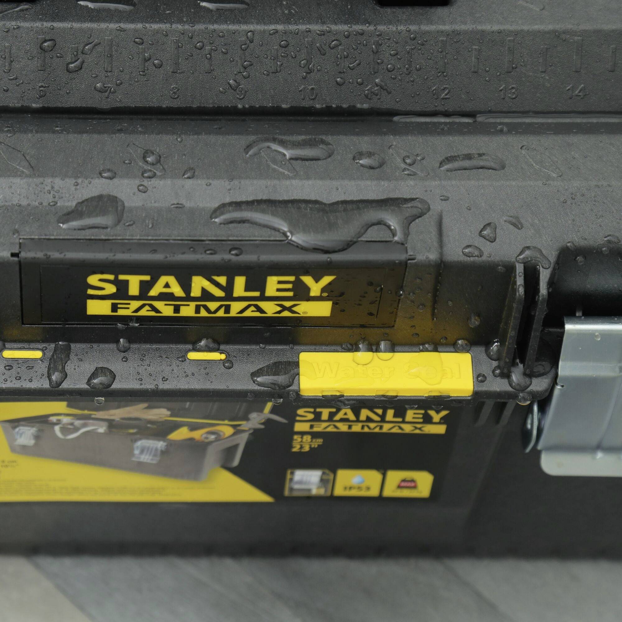 Eine schwarze Werkzeugkiste mit 'STANLEY FATMAX'-Logo und gelben Akzenten. Leicht regennass, Details einiger Werkzeuge auf dem Aufkleber.