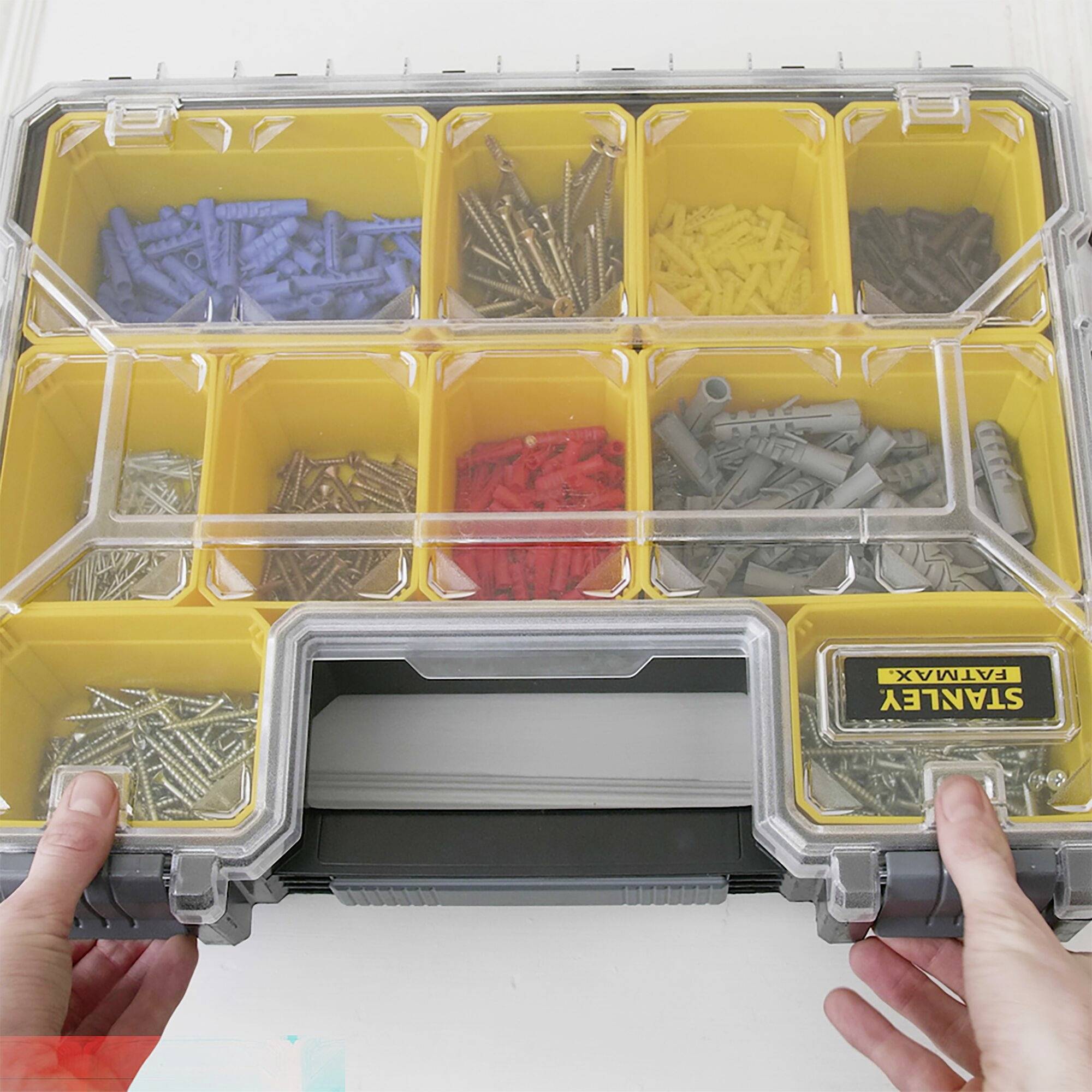 Offene Sortimentsbox mit verschiedenen Schrauben und Dübeln in gelben Fächern. Zwei Hände halten die Box.