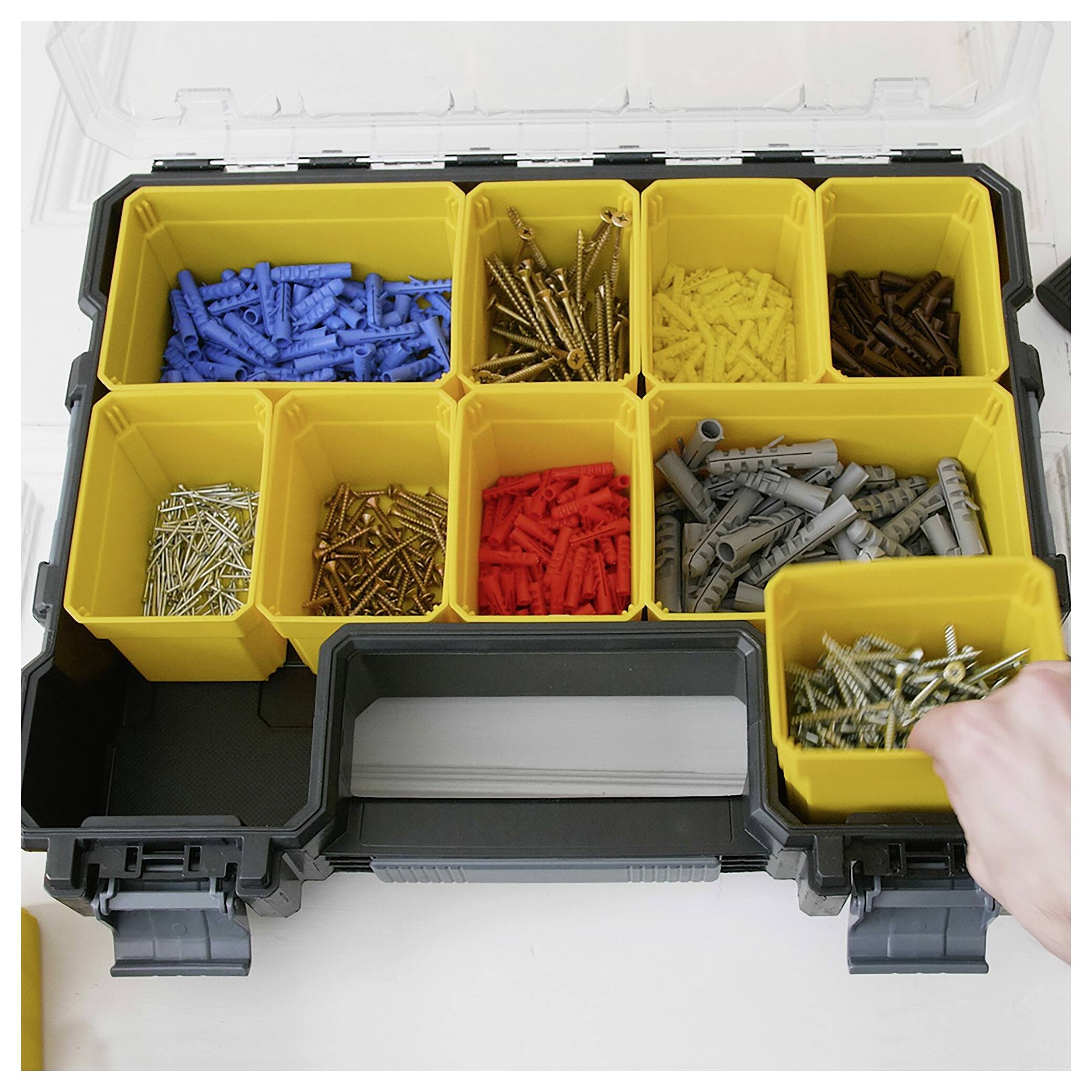 Ein geöffneter Werkzeugkasten mit mehreren Fächern. Enthält unterschiedliche Schrauben und Dübel in verschiedenen Farben und Größen. Eine Hand greift nach einem gelben Fach.