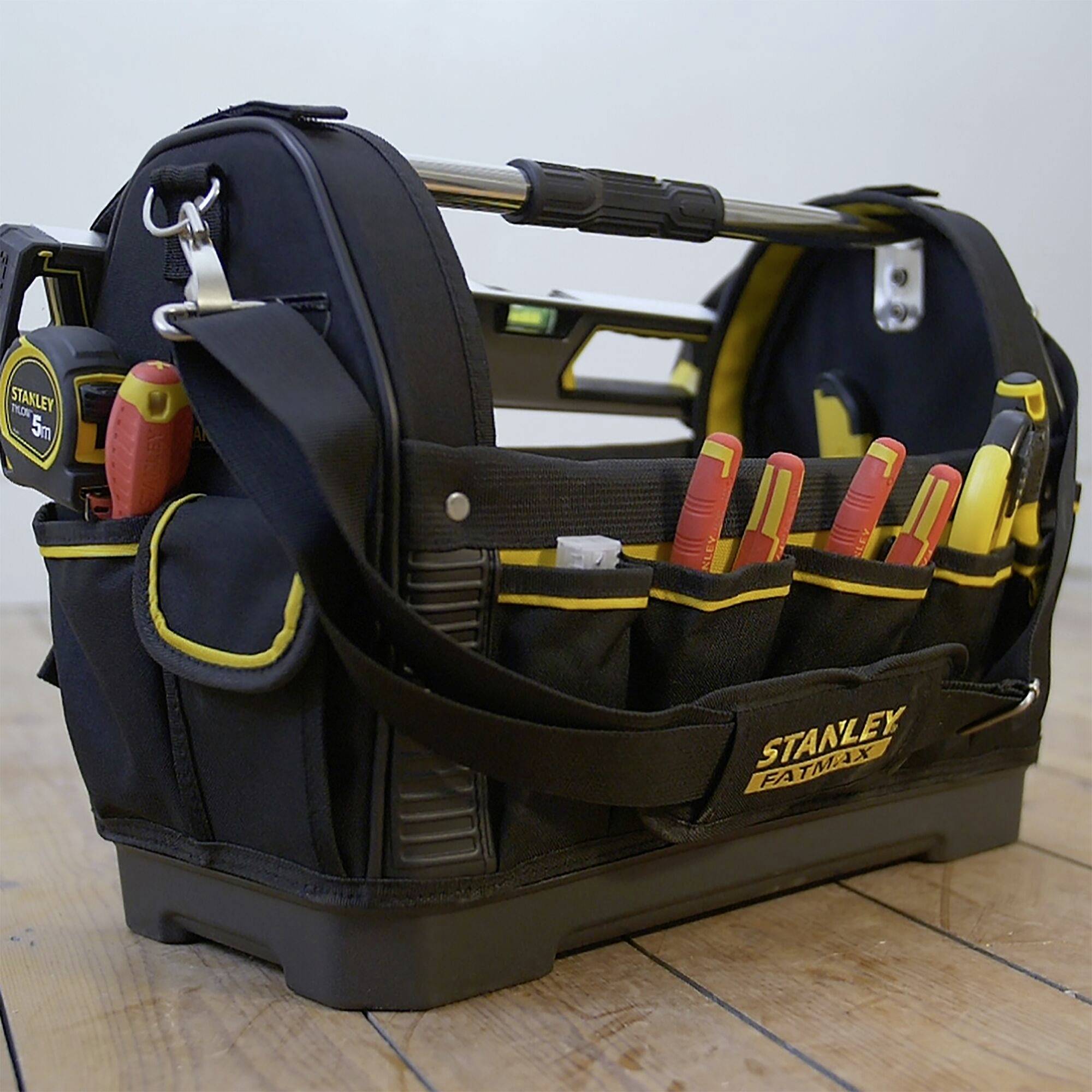Offene Werkzeugtasche auf Holzboden mit mehreren Fächern. Enthält Schraubenzieher und Maßband. Geeignet für Heimwerkerprojekte.