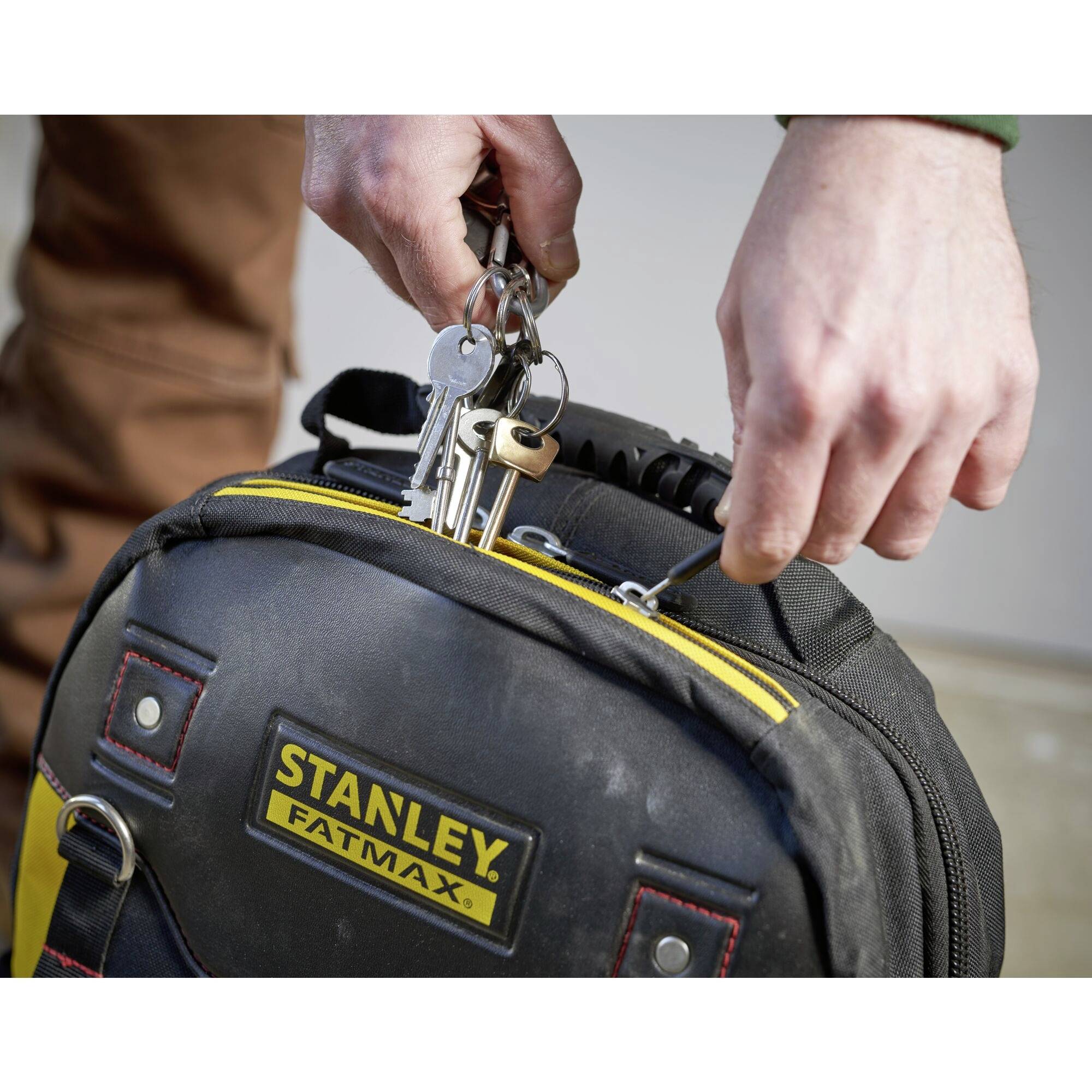 Eine Hand hält einen Schlüsselbund über einem Stanley FatMax Werkzeugrucksack.