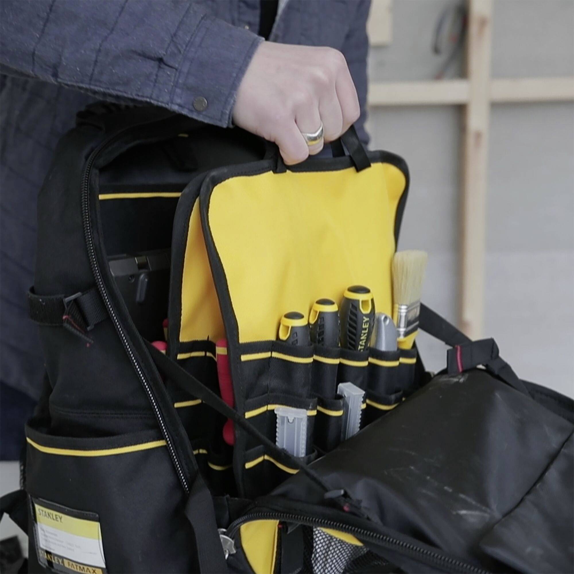 Eine Person hält eine Werkzeugtasche mit verschiedenen Werkzeugen, darunter Pinsel und Stifte, die für Handwerksarbeiten bereitstehen.