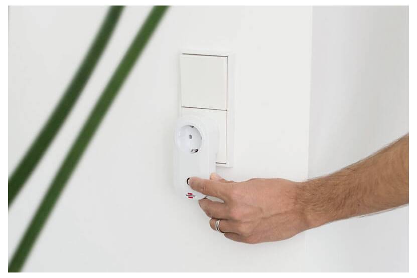 Hand dreht einen wandmontierten Thermostat oder Regelknopf an einer weißen Wand.