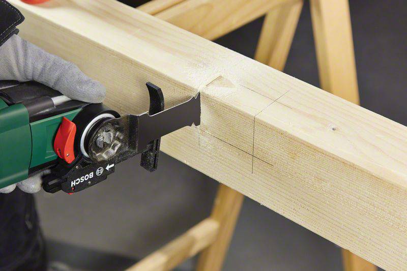 Eine Person schneidet mit einer elektrischen Säge präzise in einen Holzbalken, der auf einer Werkbank liegt.