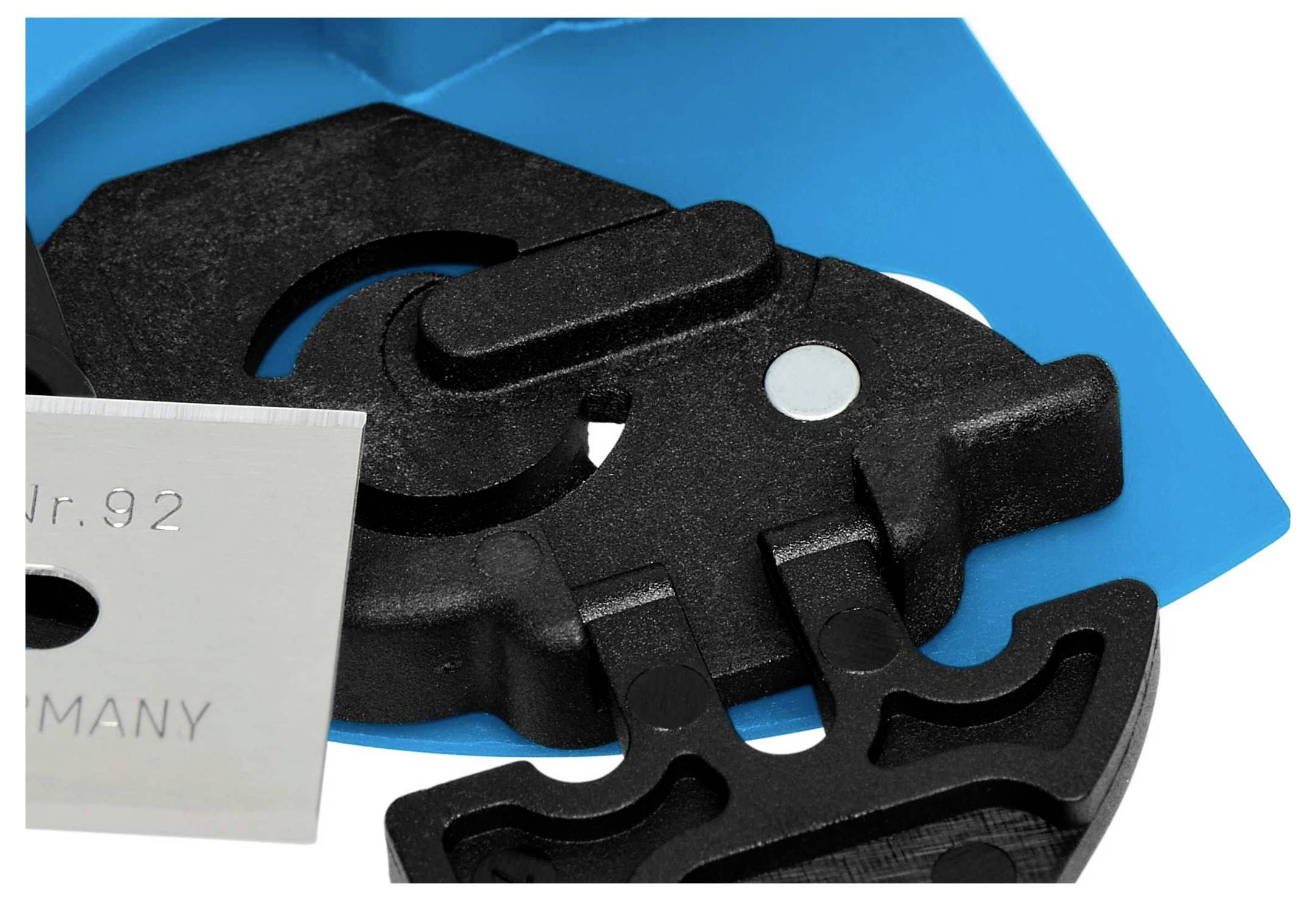 Nahaufnahme eines schwarzen Metallmechanismus auf blauem Hintergrund, zeigt Details von Zahnrädern und scharfer, silberner Klinge.