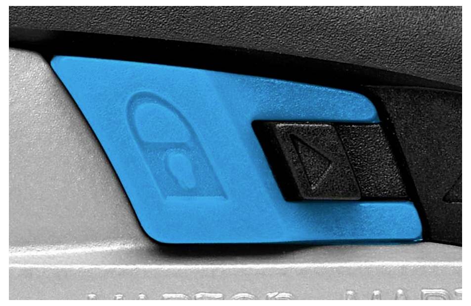 Nahaufnahme eines blauen Schalters an einem Gerät, der ein Schloss-Symbol zeigt. Der Schalter befindet sich zwischen zwei schwarzen Tasten.