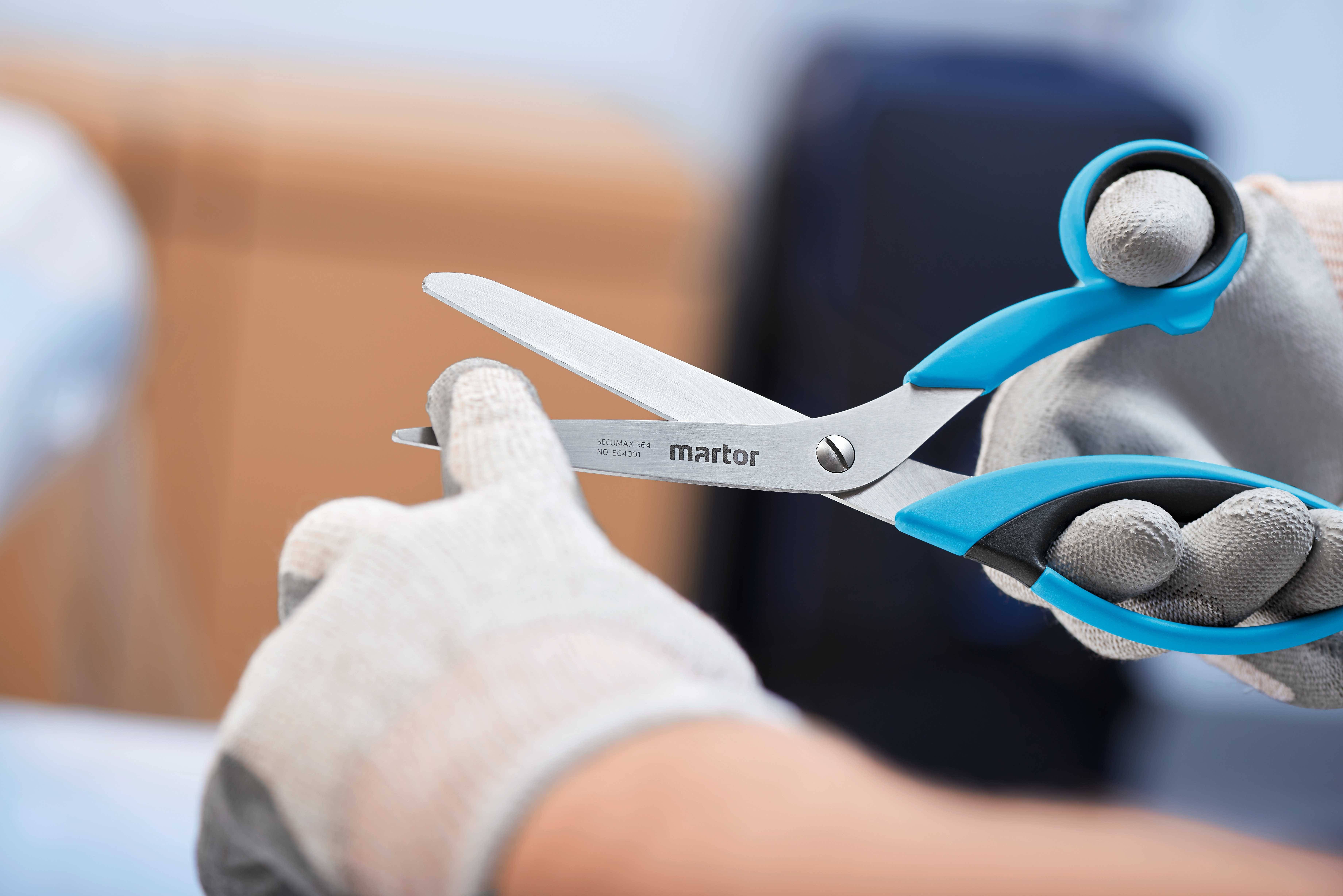 Eine Person trägt Handschuhe und hält eine Sicherheitsschere der Marke Martor, bereit zum Schneiden.