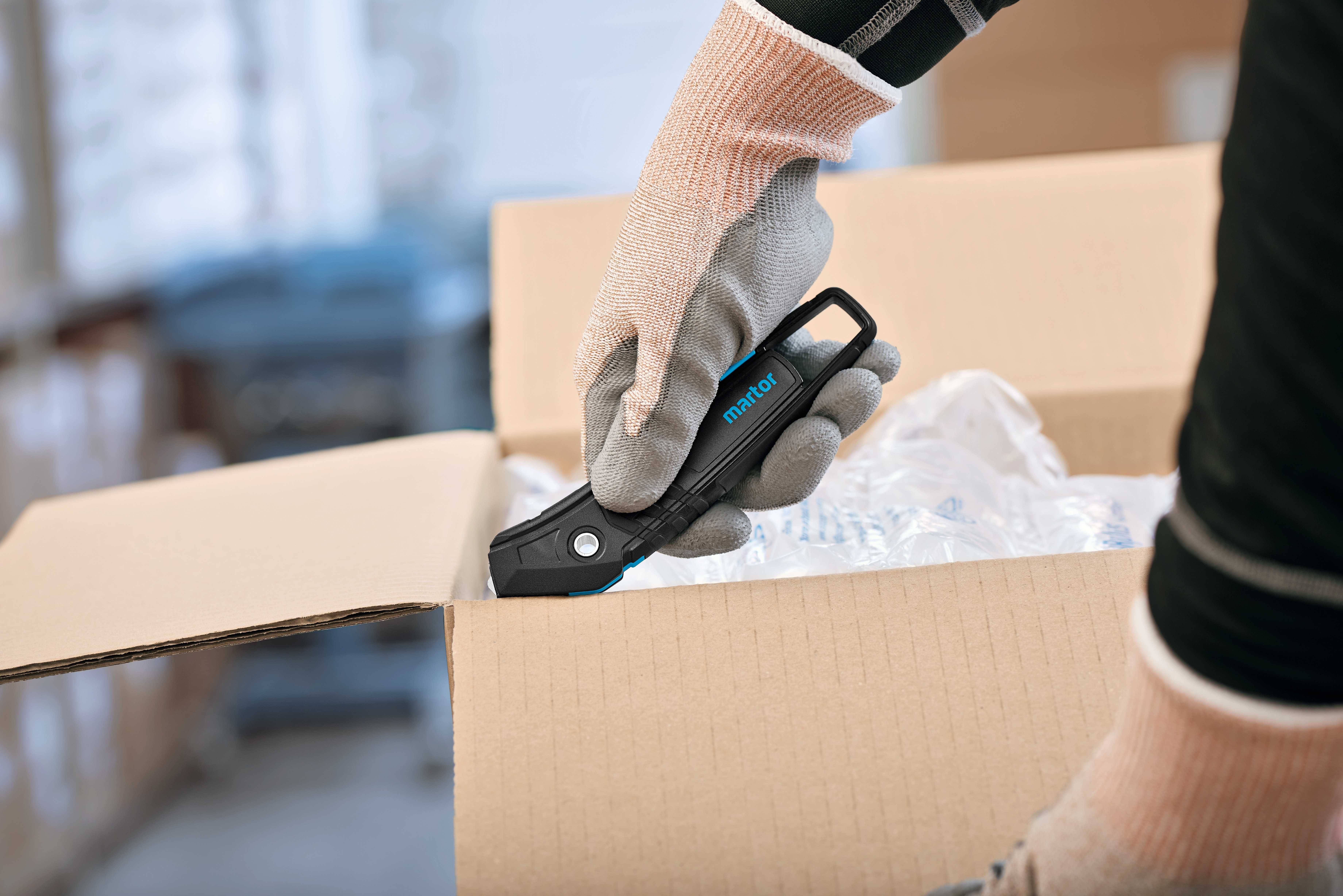 Eine Person mit Handschuhen öffnet mit einem Cutter eine Pappschachtel.