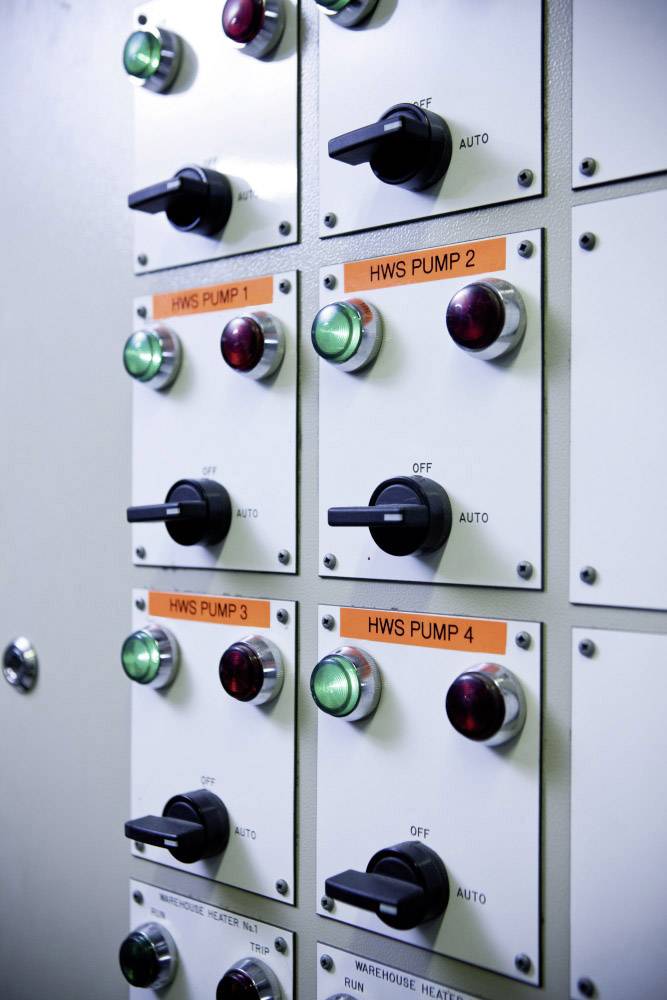 Schalttafel mit mehreren Schaltern und Lichtern, die Pumpensteuerung markieren. Etiketten zeigen 'HWS PUMP 1-4' an. Schalter auf 'Auto' oder 'Off'.