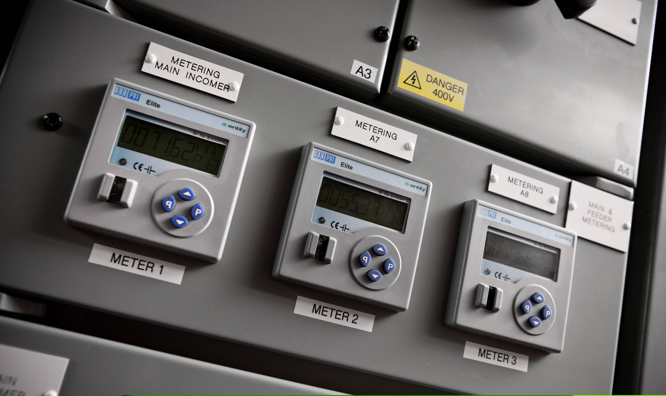 Drei digitale Stromzähler an einer grauen Schalttafel, darunter der Text 'Metering Main Incomer' und Warnhinweis 'Danger 400V'.