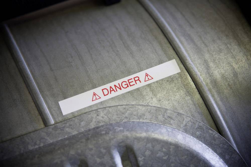 Ein Warnschild mit roter Aufschrift 'DANGER' und Gefahrensymbolen auf einer Metalloberfläche weist auf mögliche Risiken hin.