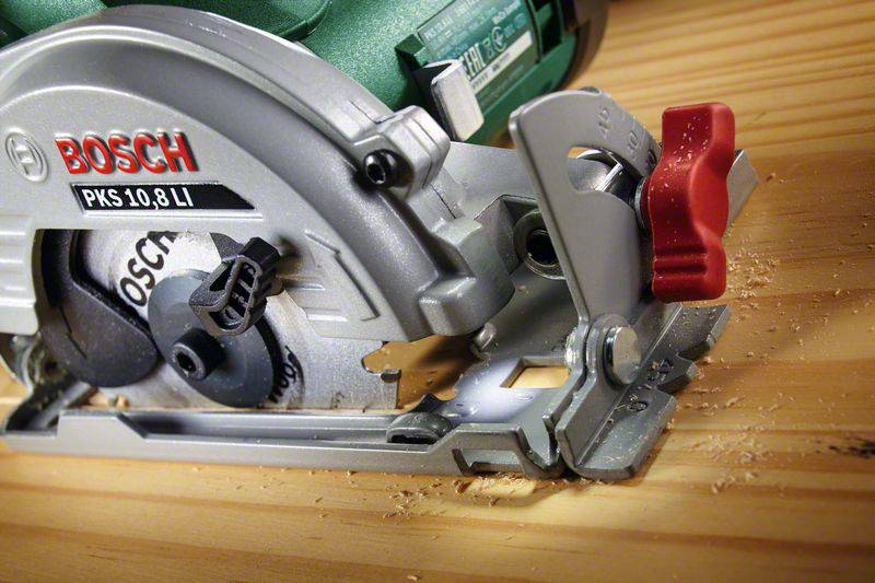 Nahaufnahme einer Handkreissäge während des Schneidens von Holz. Der Sägeblatt ist sichtbar und Holzspäne sind um das Werkstück verstreut.