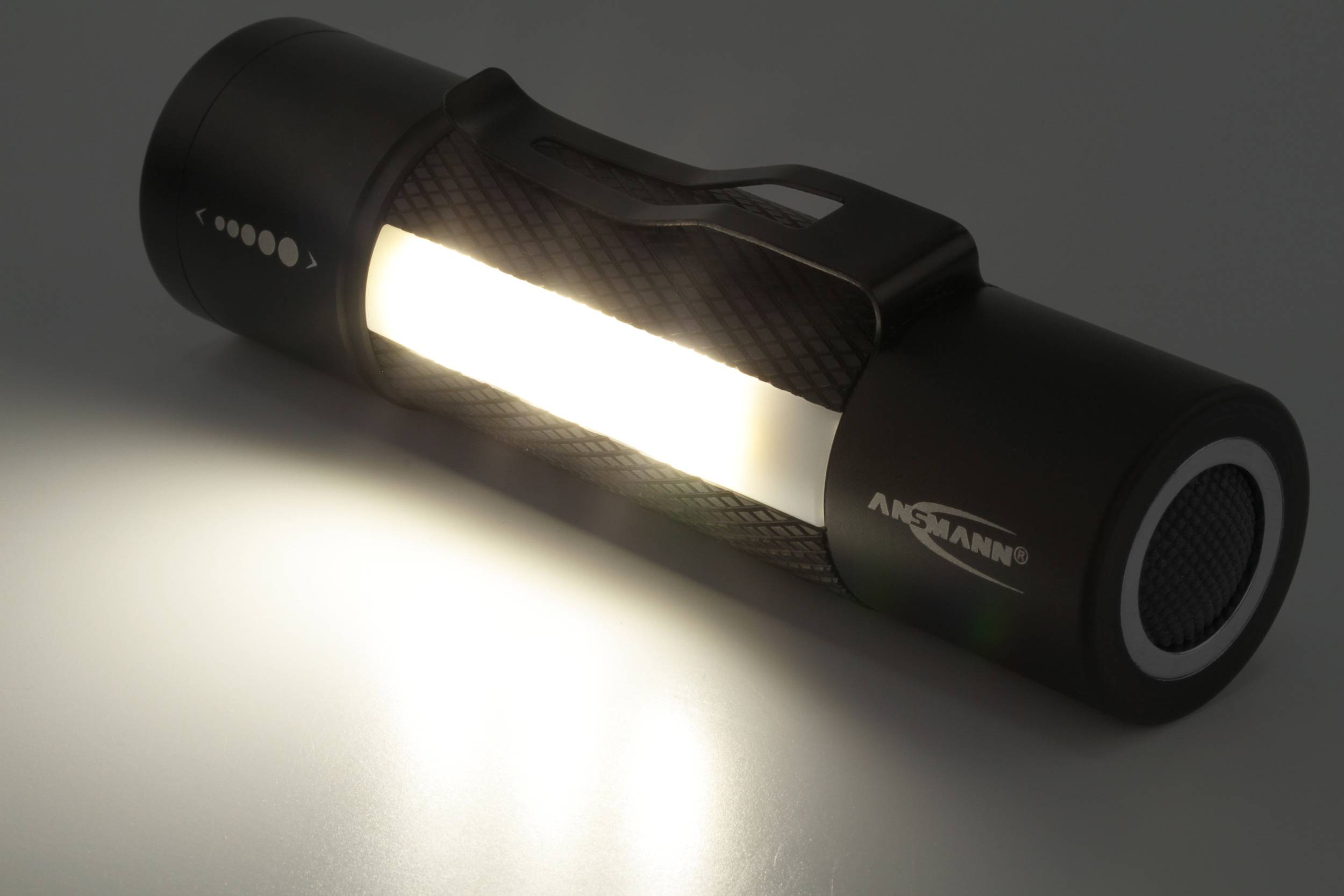 Eine tragbare, schwarze Taschenlampe liegt auf einer Oberfläche und strahlt helles Licht aus.
