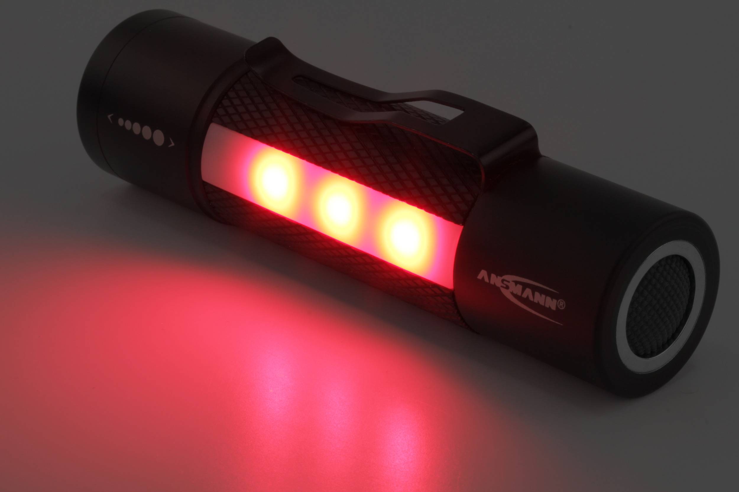 Eine schwarze Taschenlampe leuchtet mit drei roten LEDs in der Dunkelheit.