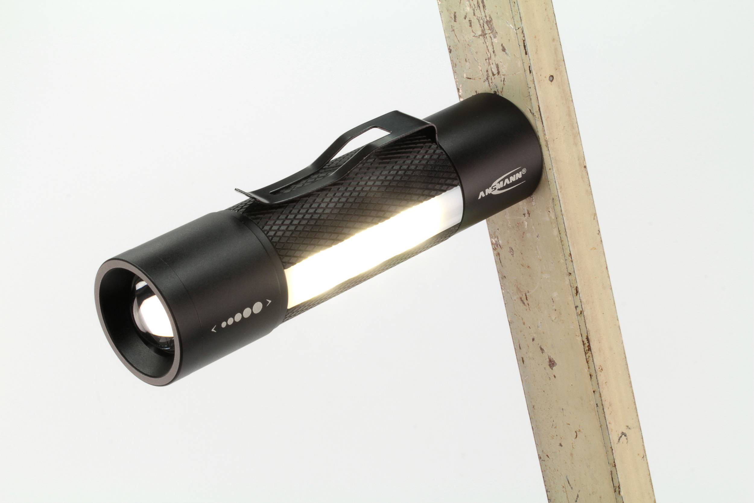 Eine schwarze Taschenlampe mit leuchtendem Licht, die an einem schrägen Holzstück befestigt ist. Sie hat eine rutschfeste Oberfläche.