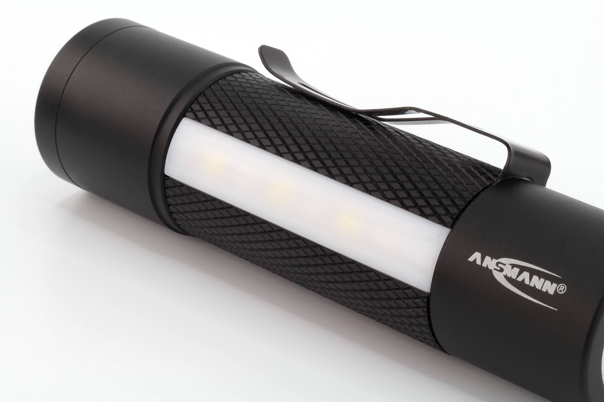 Schwarze Taschenlampe mit strukturiertem Griff und Clip, weißer Leuchtbereich, Markenname 'ANSMANN' sichtbar.
