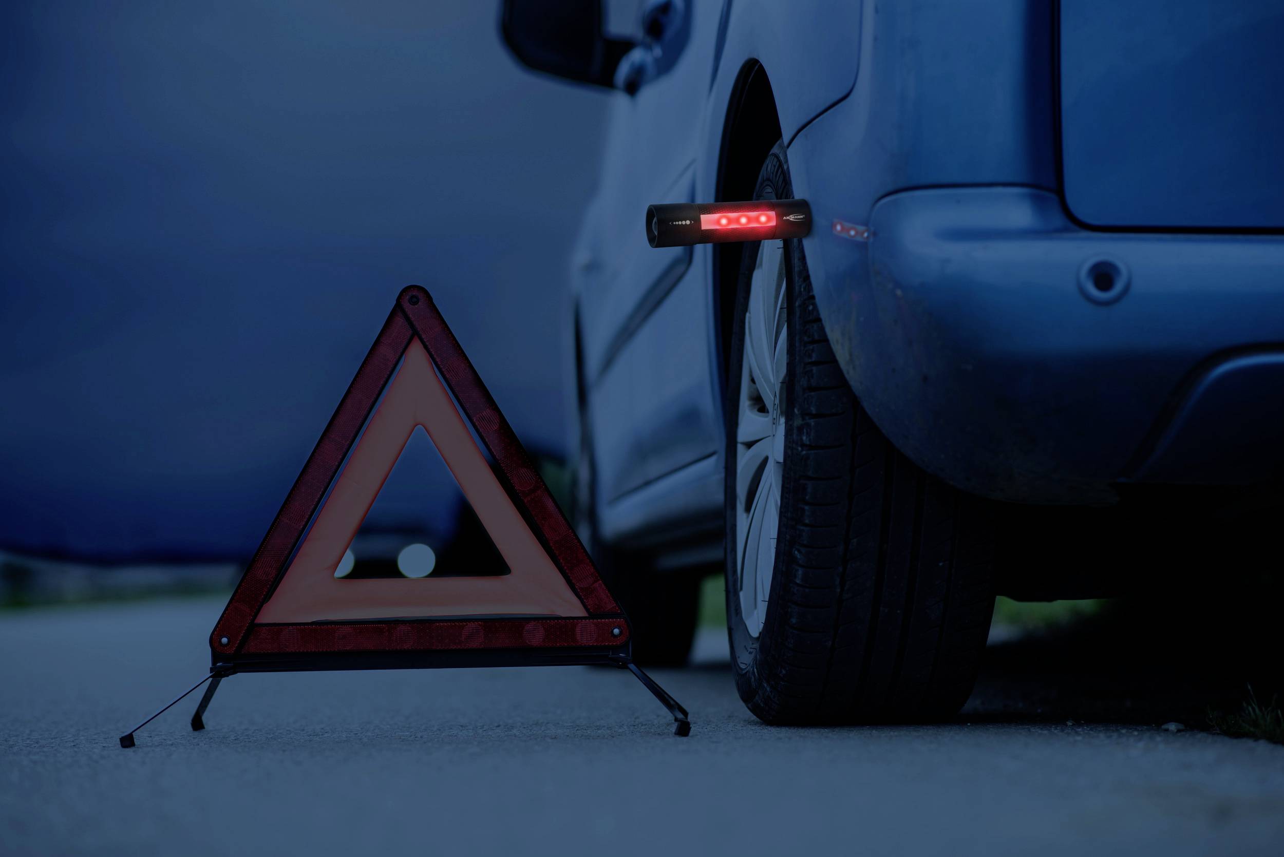Ein warnblinkendes Dreieck steht nahe einem am Straßenrand geparkten Auto bei Dämmerung, um vor einer möglichen Gefahr zu warnen.
