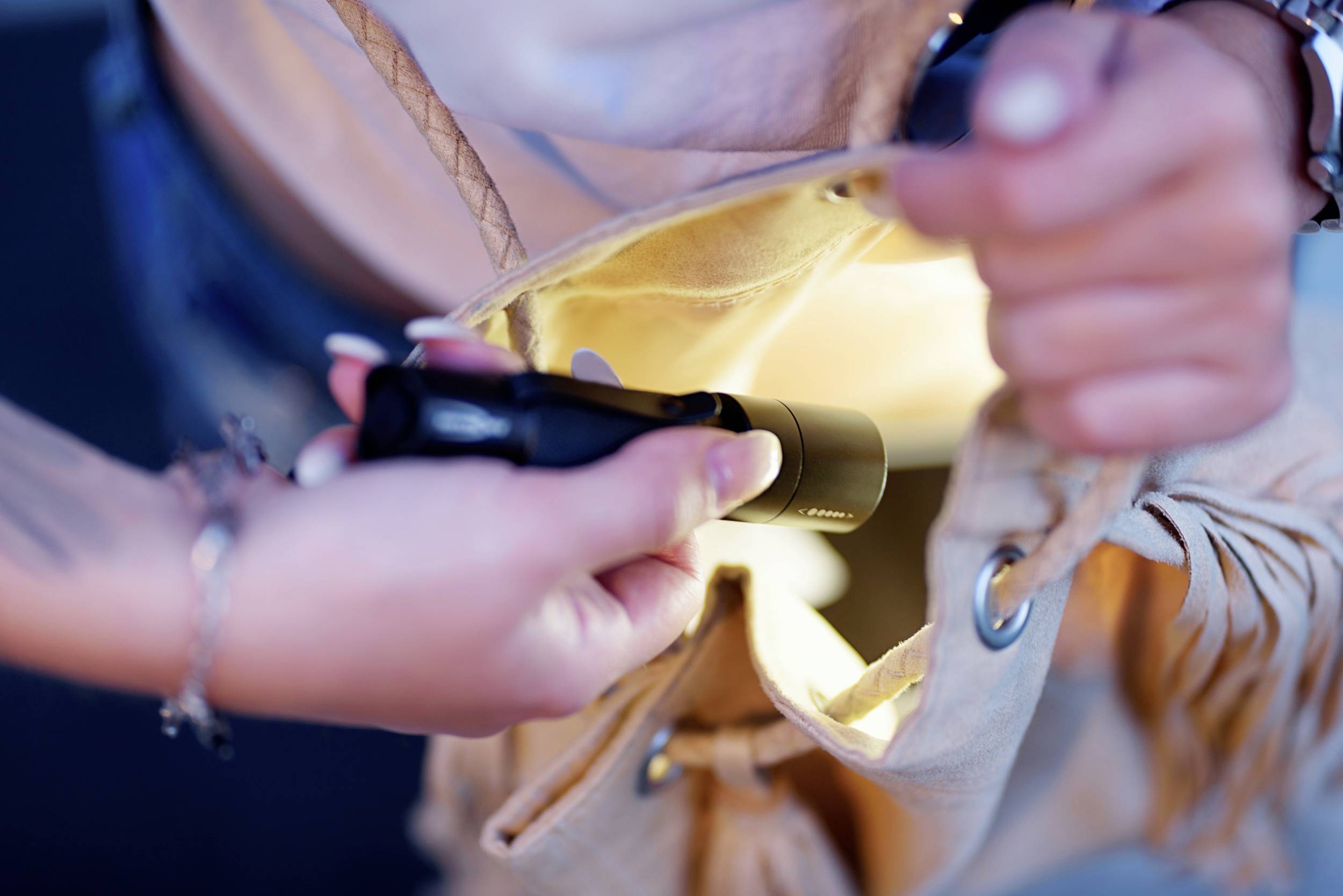 Person öffnet Tasche, in die mit einer kleinen Taschenlampe geleuchtet wird. Die Szene zeigt eine konzentrierte Suche nach einem Gegenstand.