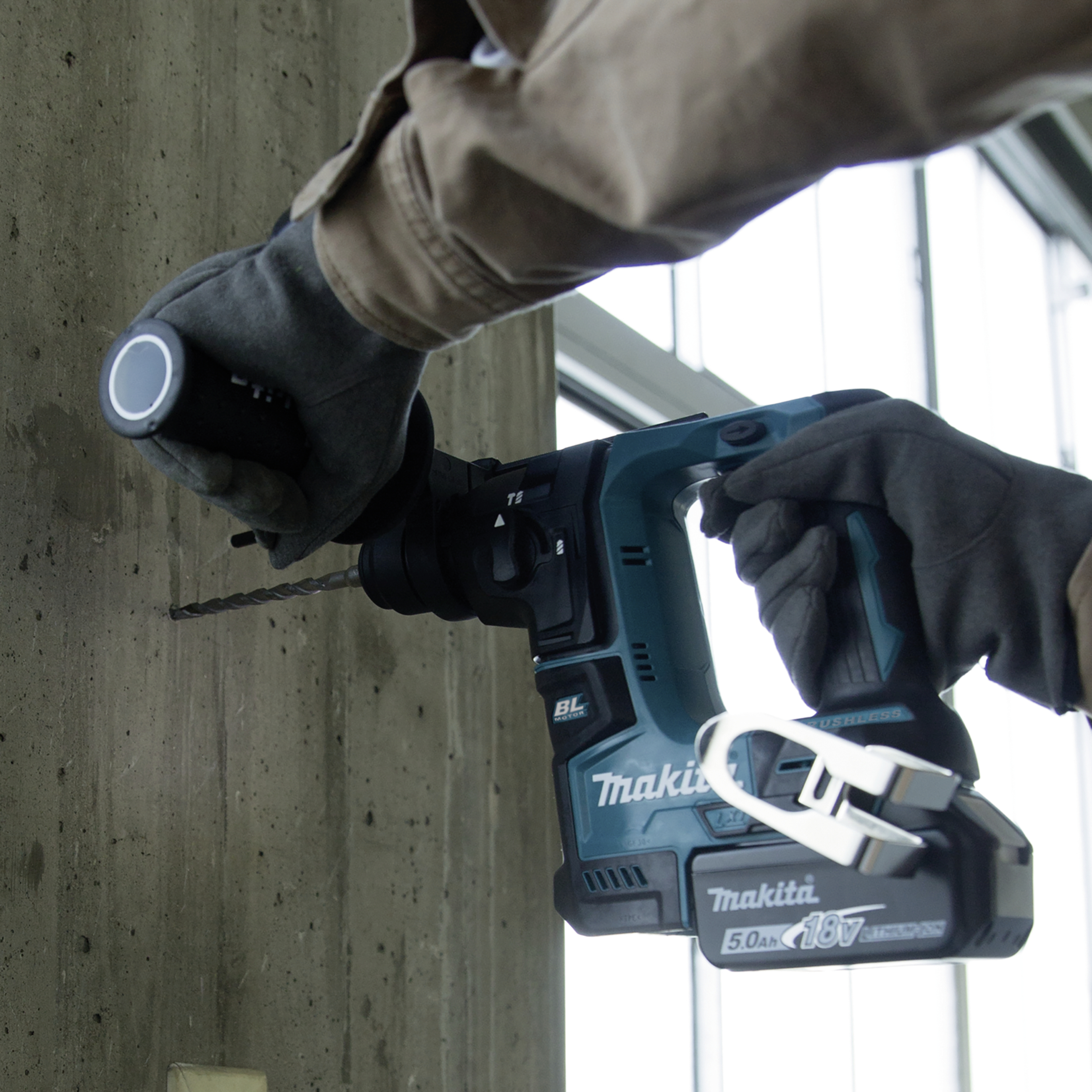 Person bohrt mit blauem Akkubohrhammer in eine Betonwand.