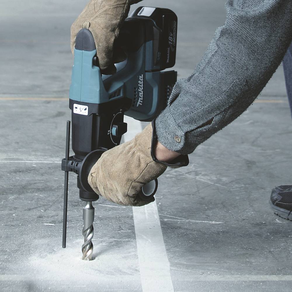 Eine Person trägt Arbeitshandschuhe und bedient eine elektrische Bohrmaschine auf einer Betonfläche.