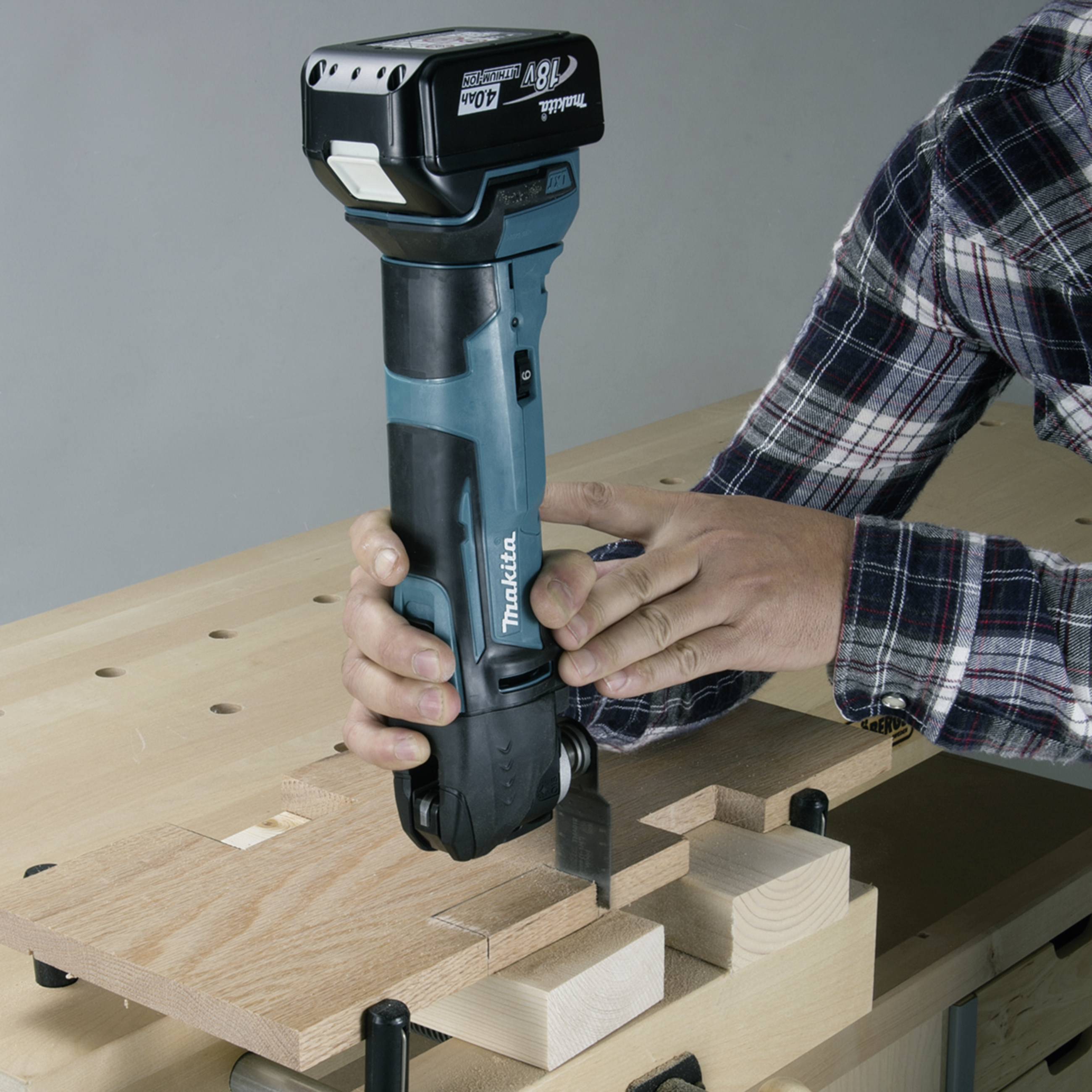 Eine Person bearbeitet Holz mit einem blauen Akku-Schleifer an einem Werkbank.