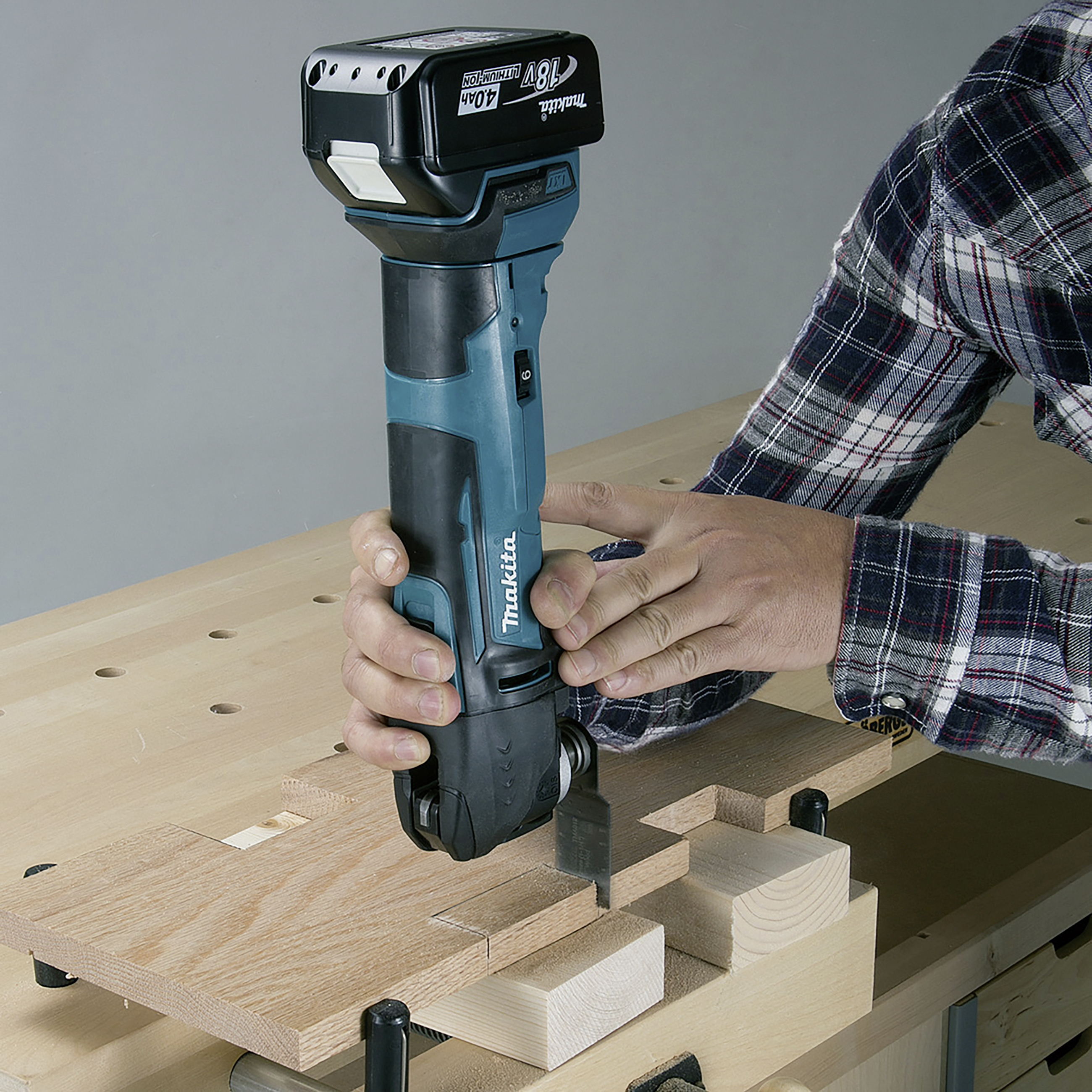 Eine Person arbeitet mit einem blauen Elektrowerkzeug auf einer Holzoberfläche, um Holzstücke präzise zu schneiden.