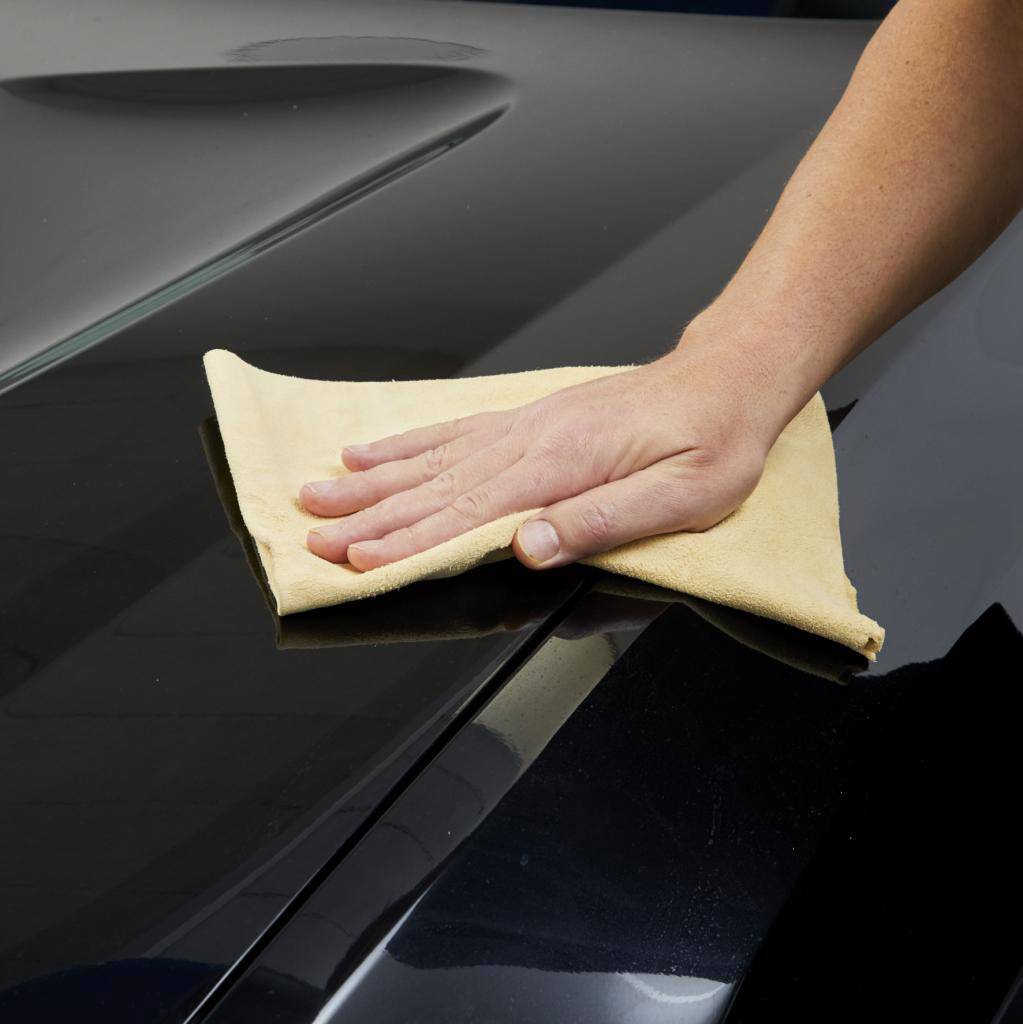 Eine Hand wischt mit einem gelben Tuch über den glänzenden Lack eines schwarzen Autos.