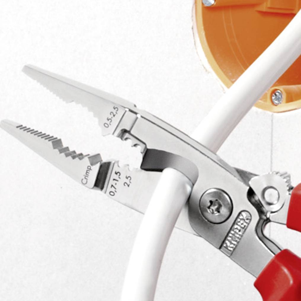 Eine Zange hält zwei weiße Kabel vor einer orangefarbenen Buchse.