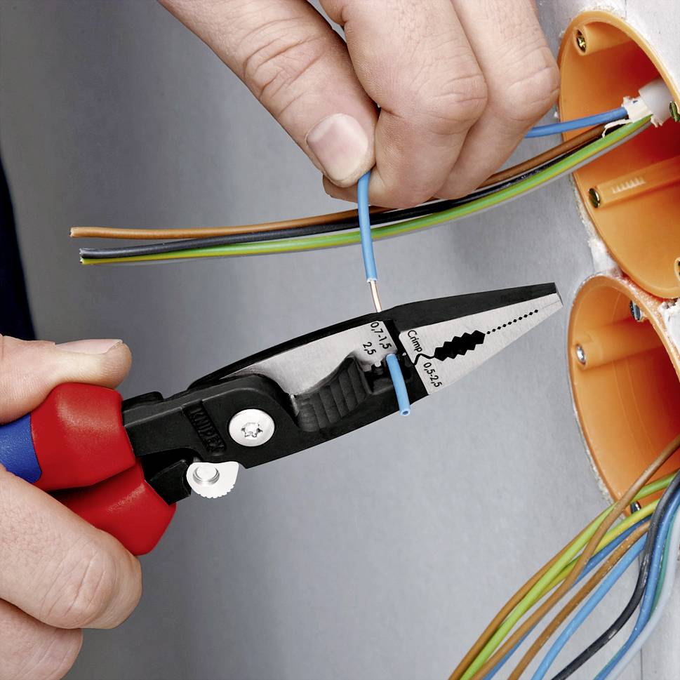 Ein Handwerker klemmt mit Zange die Enden von elektrischen Kabeln in einer orangefarbenen Dose ein. Einbau einer Elektroinstallation.