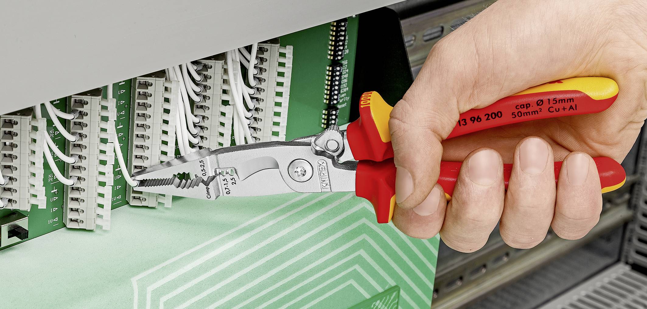 Eine Hand benutzt einen isolierten Seitenschneider, um ein Kabel in einer elektrischen Schalttafel abzuziehen.