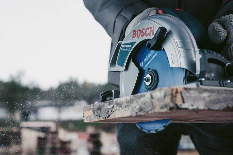 Ein Handwerker schneidet mit einer Bosch-Kreissäge durch ein Holzbrett. Sägespäne fliegen im Hintergrund.