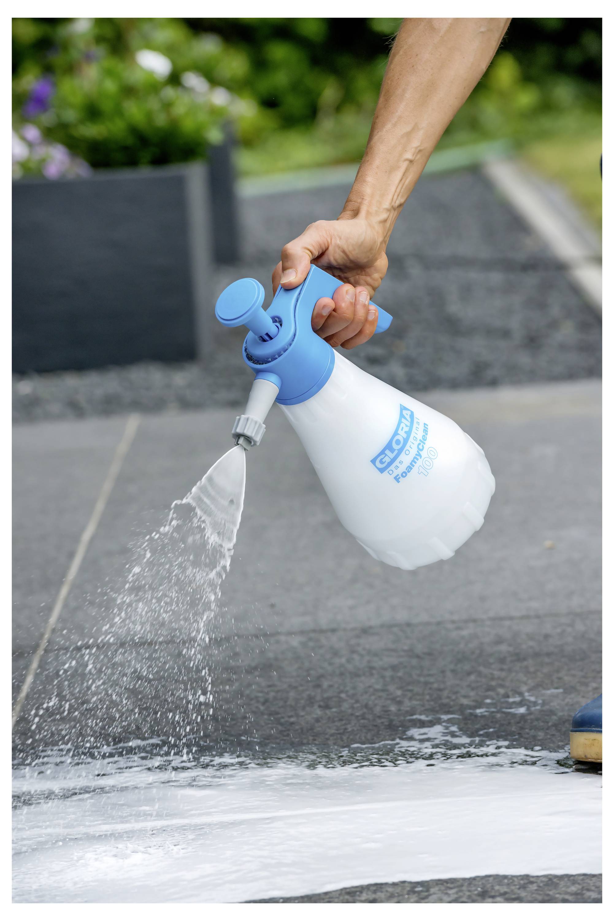 Mit einem blau-weißen Drucksprüher weiß Reinigungsschaum von Hand auf eine Gehweg- oder Betonoberfläche im Freien sprühen.