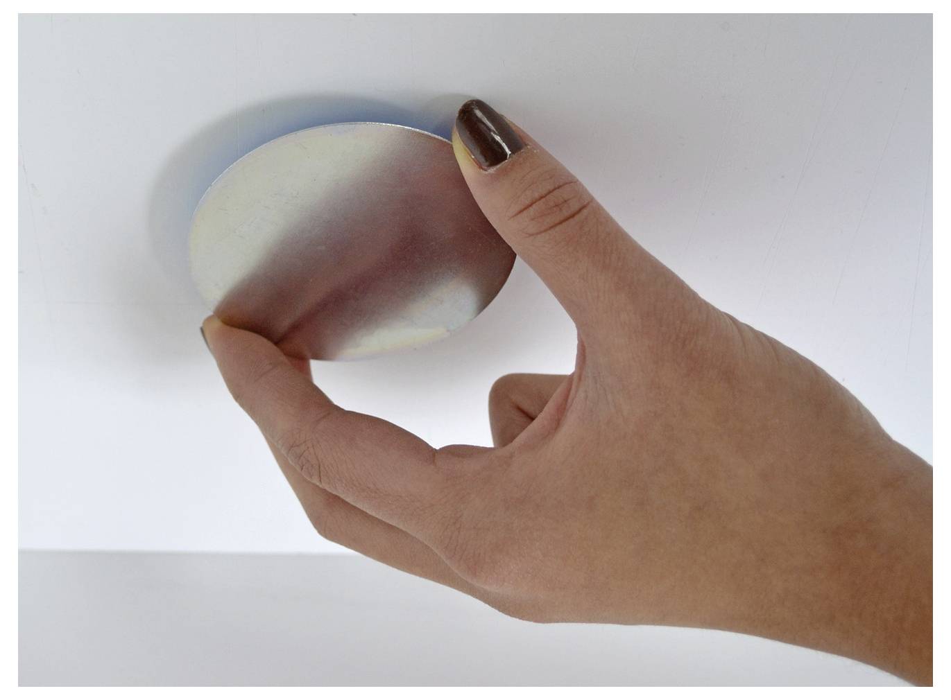Eine Hand drückt einen abgerundeten weiß-rosa Stressball gegen eine weiße Oberfläche.