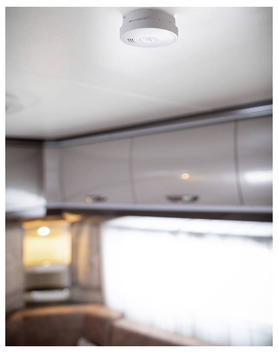 Rauchmelder an der Decke eines Wohnmobilinneren montiert, mit Schränken, einem Fenster und Sitzplätzen darunter.