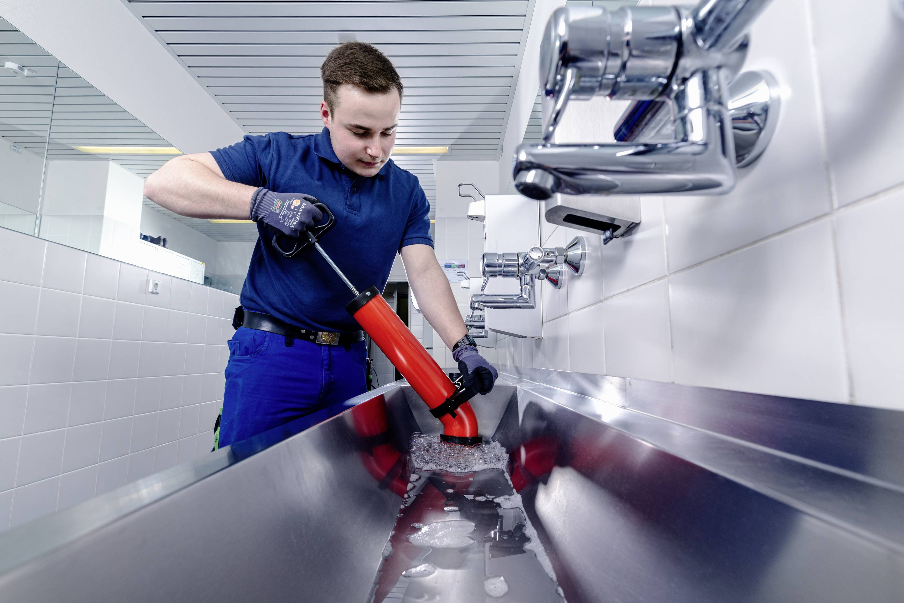Ein Installateur mit blauer Uniform arbeitet an einem Waschbecken und verwendet eine Saugglocke, um einen Abfluss zu reinigen.